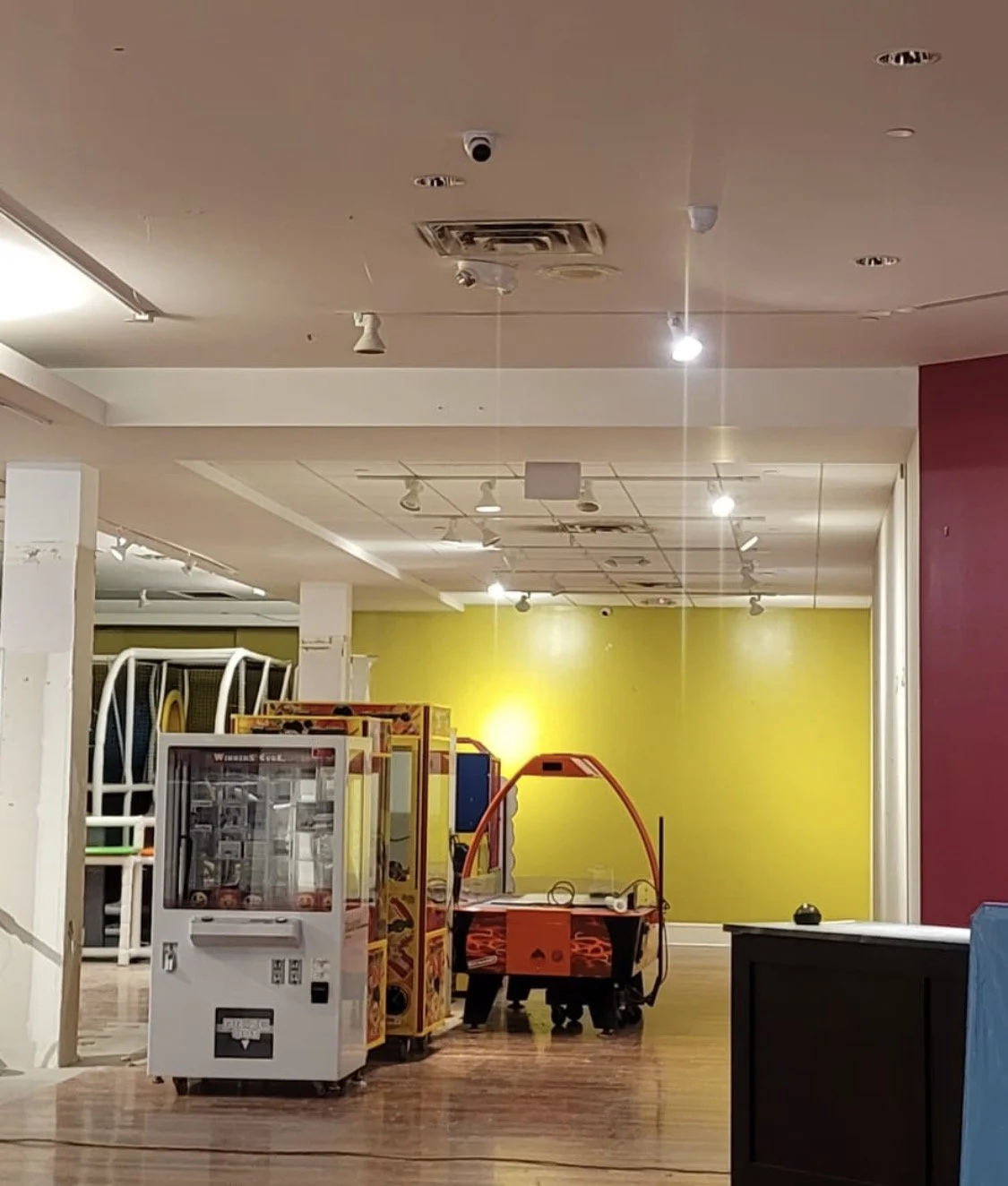 Interior of an arcade or entertainment center with claw machines and a yellow wall in the background.