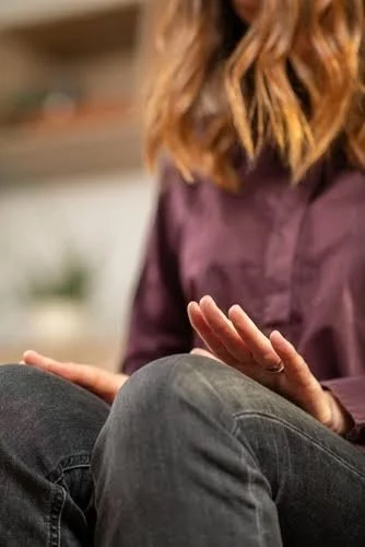Close-up of two people sitting, with one person gesturing with their hand, wearing a purple shirt and jeans.