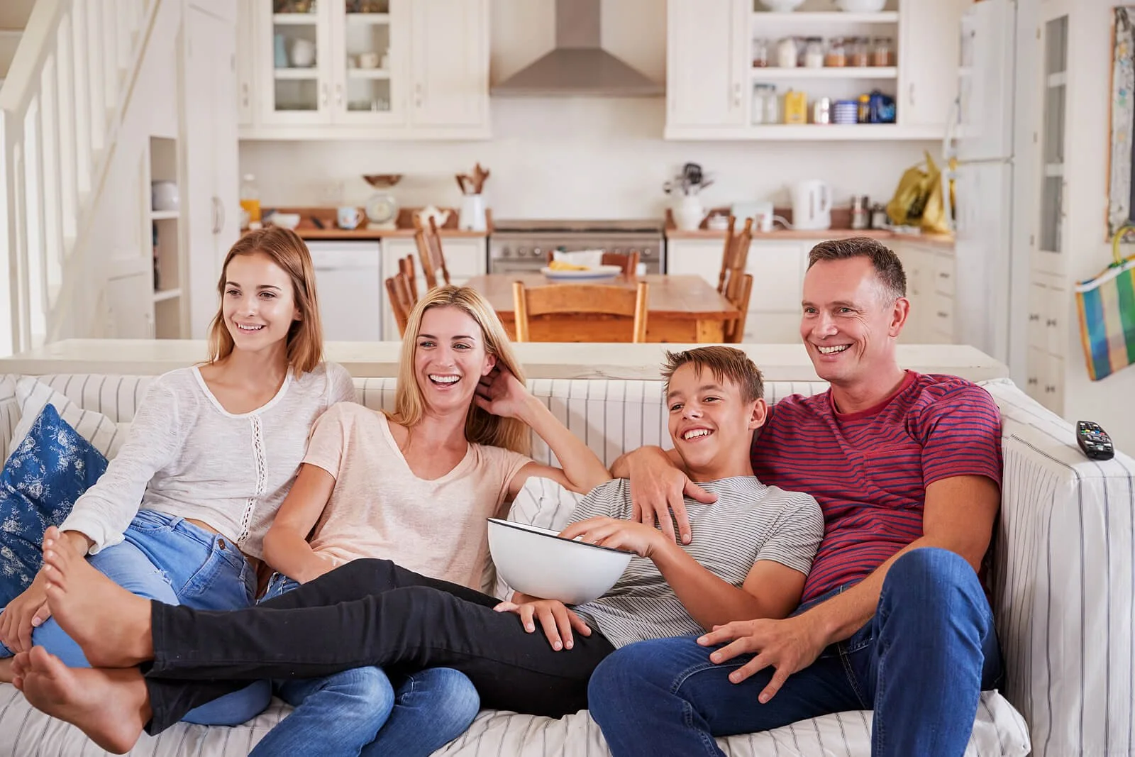 A family with two teenagers sitting together & watching a movie in a bright lit room. Learn how teen therapy in Miami, FL can support your family. Start therapy for the whole family today.