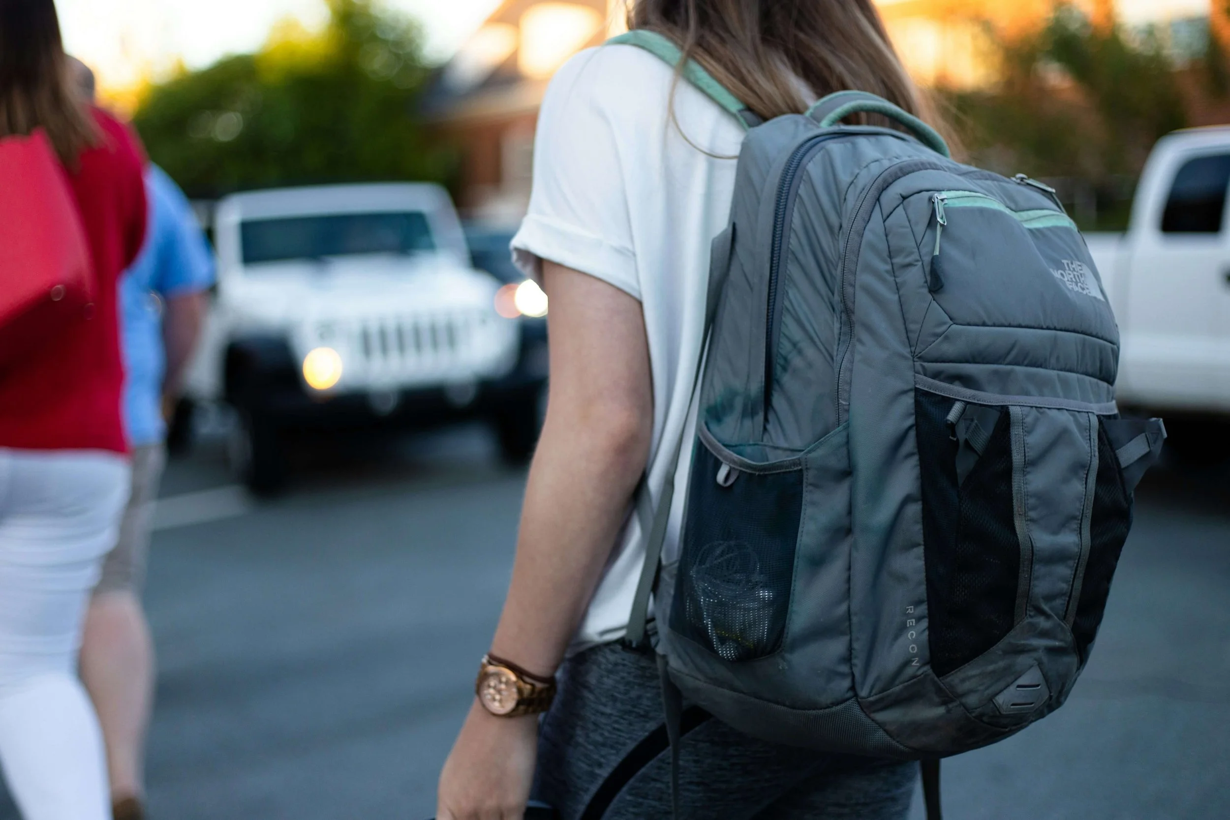 A teenager wearing a gray North Face backpack walking in a school parking lot. Teen counseling in Miami, FL is here to support teenagers with executive functioning, emotional regulation & exam stress.