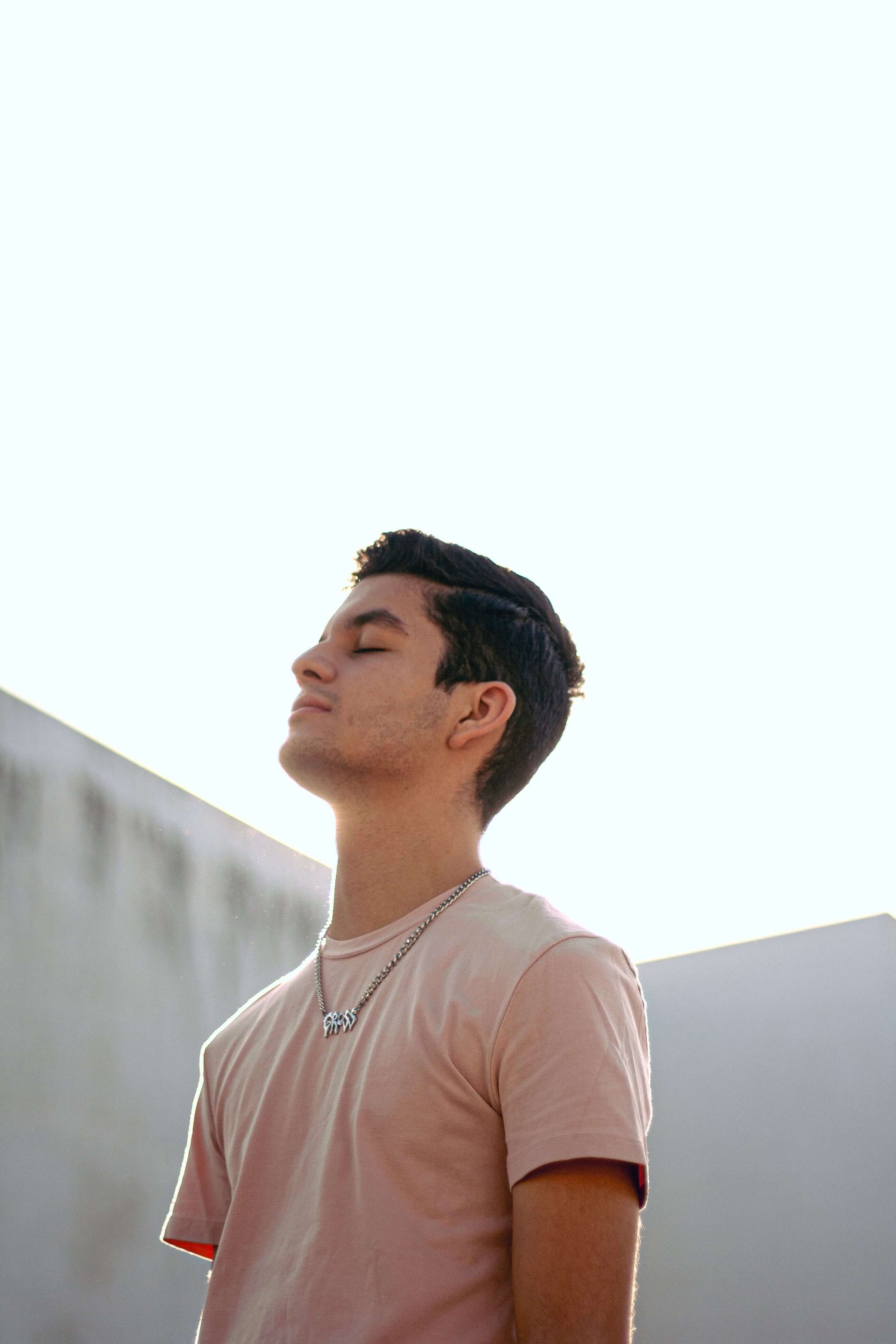 A teen boy wearing a light pink shirt closing his eyes outside. This represents teen mindfulness & the dbt skills. Teen therapy in Miami, FL can help your teen navigate big emotions.