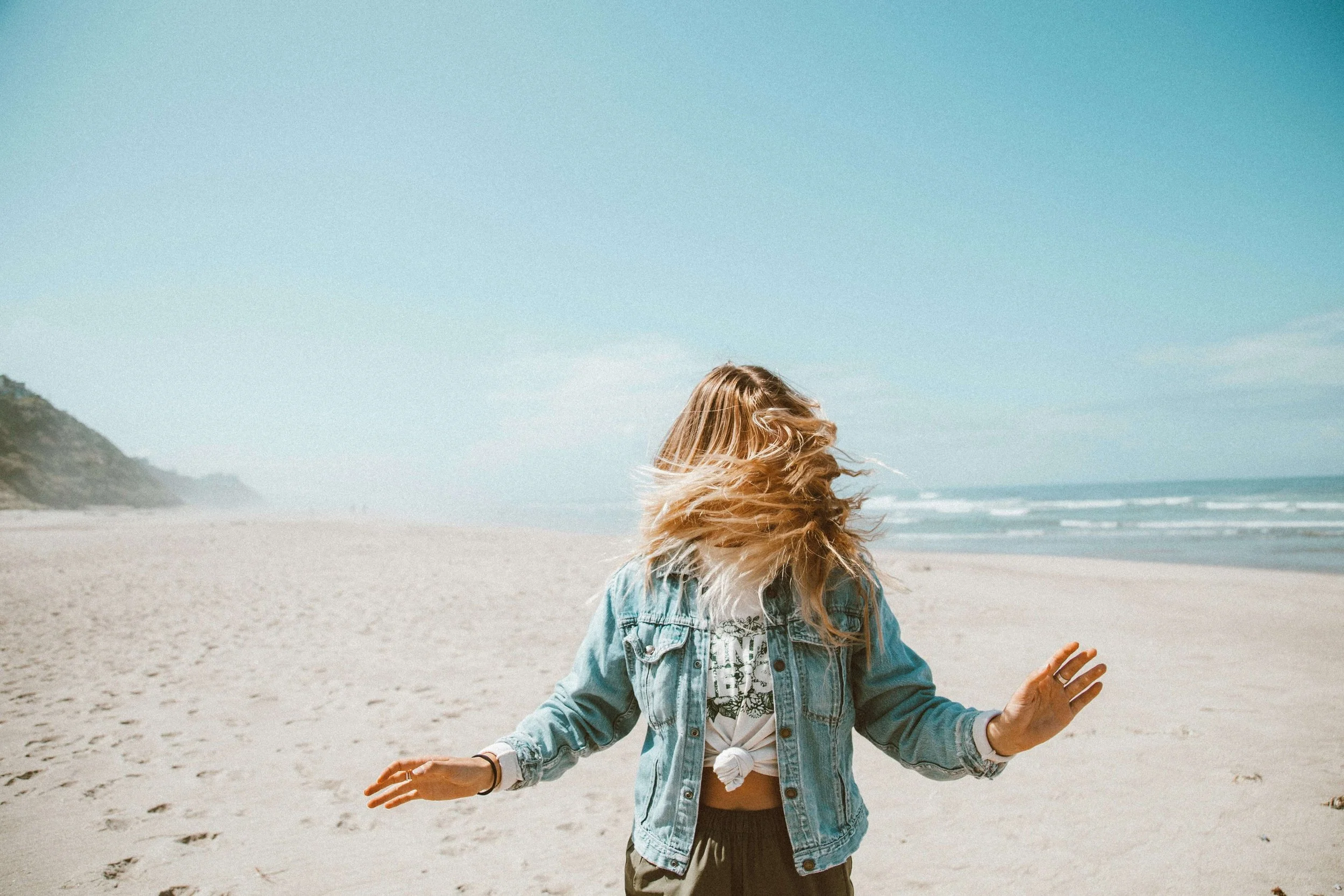 A teen girl walking backwards on the beach while her hair flows over her face. Helping your teen keep a routine in the summer is important for emotional regulation & mental health. Discover how working with a teen therapist in Miami, FL can help.