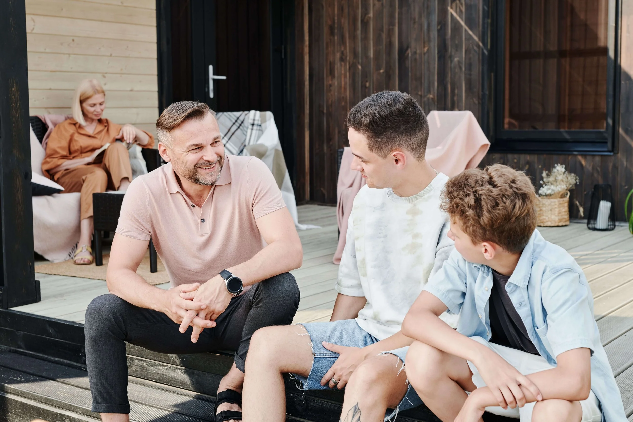 A father sitting next to his two teen sons outside on the patio, talking. Teen therapy in Miami, FL can help with emotional regulation, ADHD & routine. Learn more here!