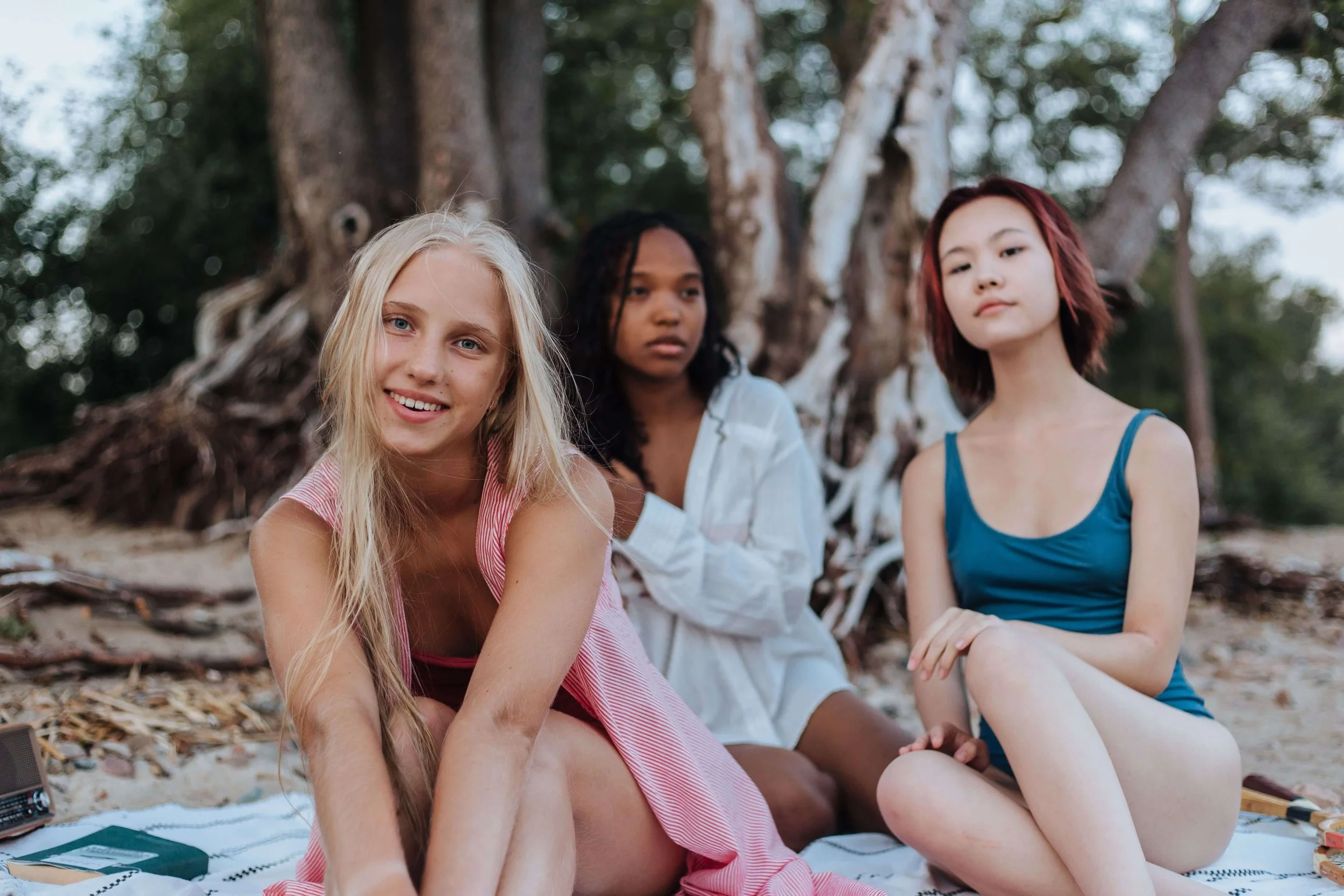 A group of diverse teen girls sitting on a beach together near trees. If your teen struggles with anxiety, learn how teen therapy in Miami, FL can help them navigate it in a safe space. Learn more about teen anxiety here.