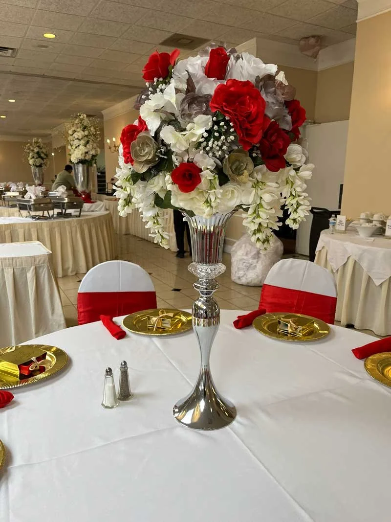 A floral centerpiece on a banquet table featuring white, red, and cream flowers with greenery in a silver vase, set for a formal event.