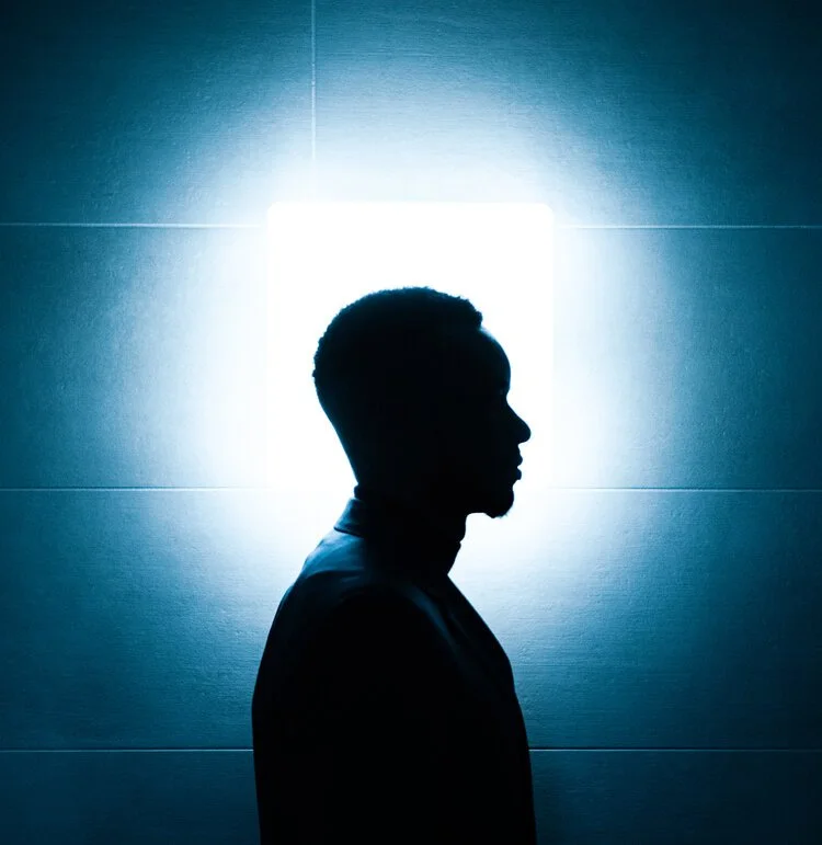 An editorial style photo of Styled by Barnet, the silhouette of his side profile encapsulated by white light and blue shadows, matching his blue suit.