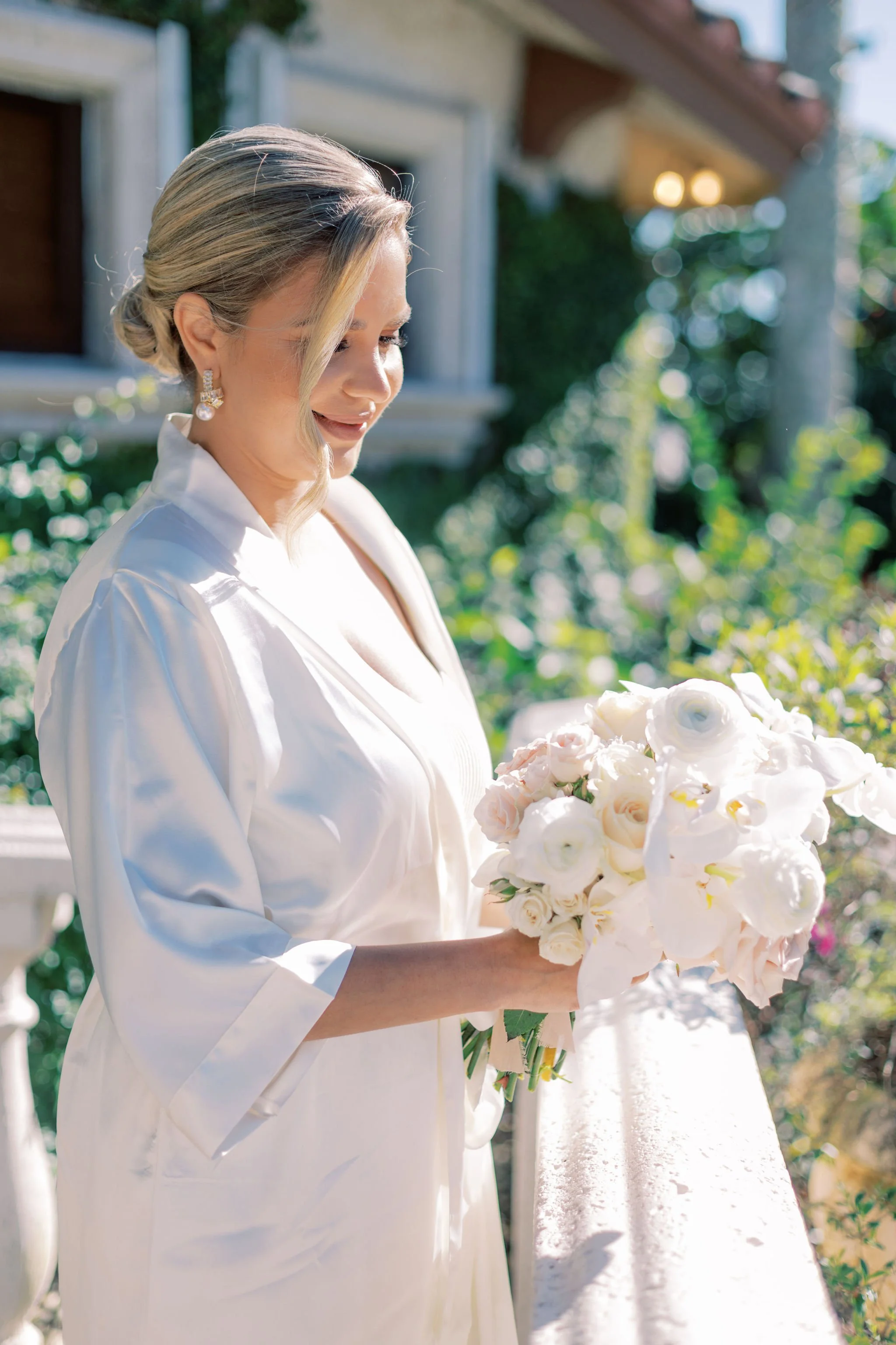 Woman in white robe holding a bouquet of flowers outdoors
