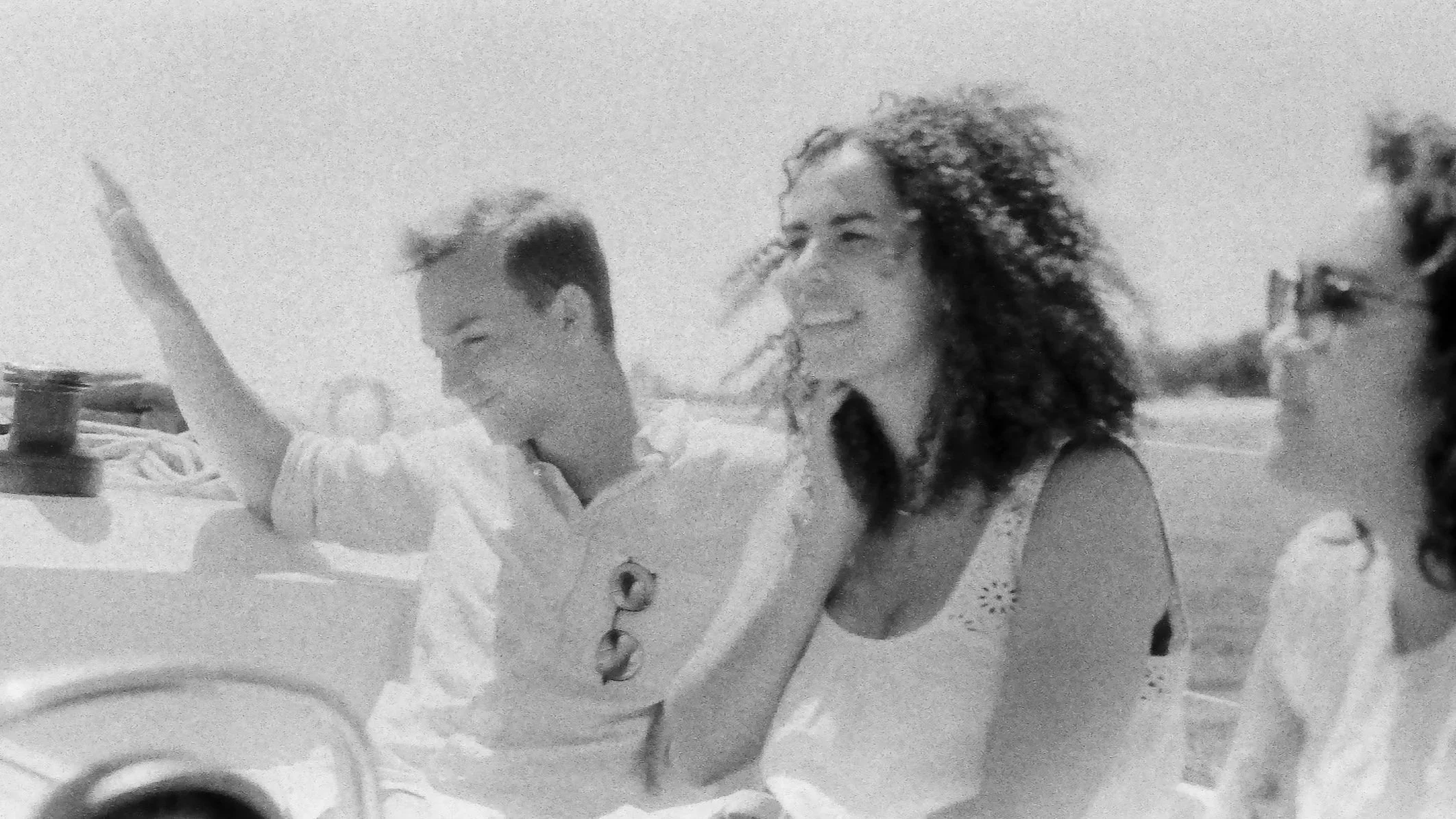 Three people, two women and a man, are sitting together outdoors on a sunny day, smiling and enjoying each other's company.