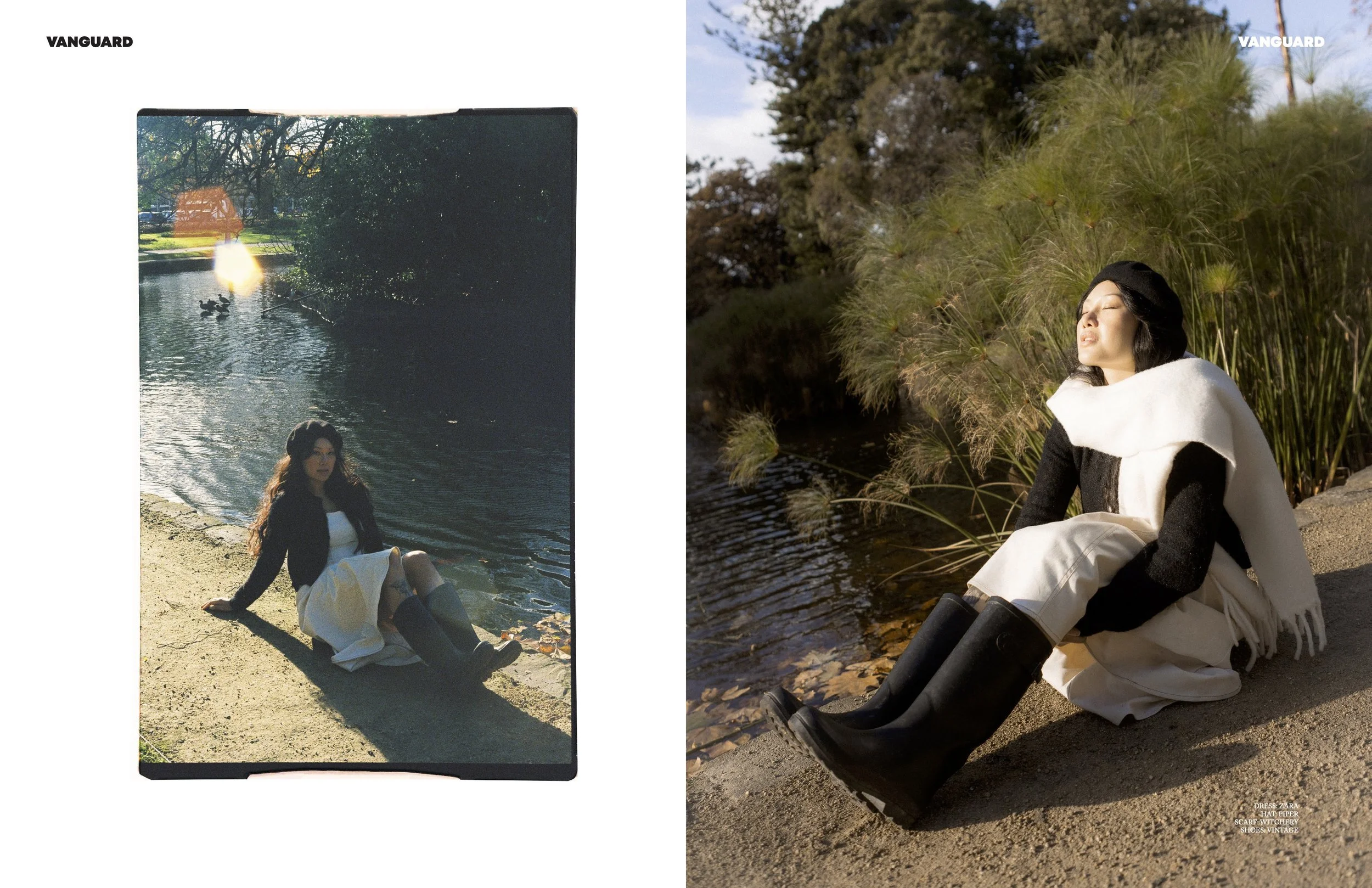 A woman sitting by a riverbank with tall grasses, wearing a black hat, black and white clothing, and black boots, with her eyes closed and face tilted upward in sunlight.