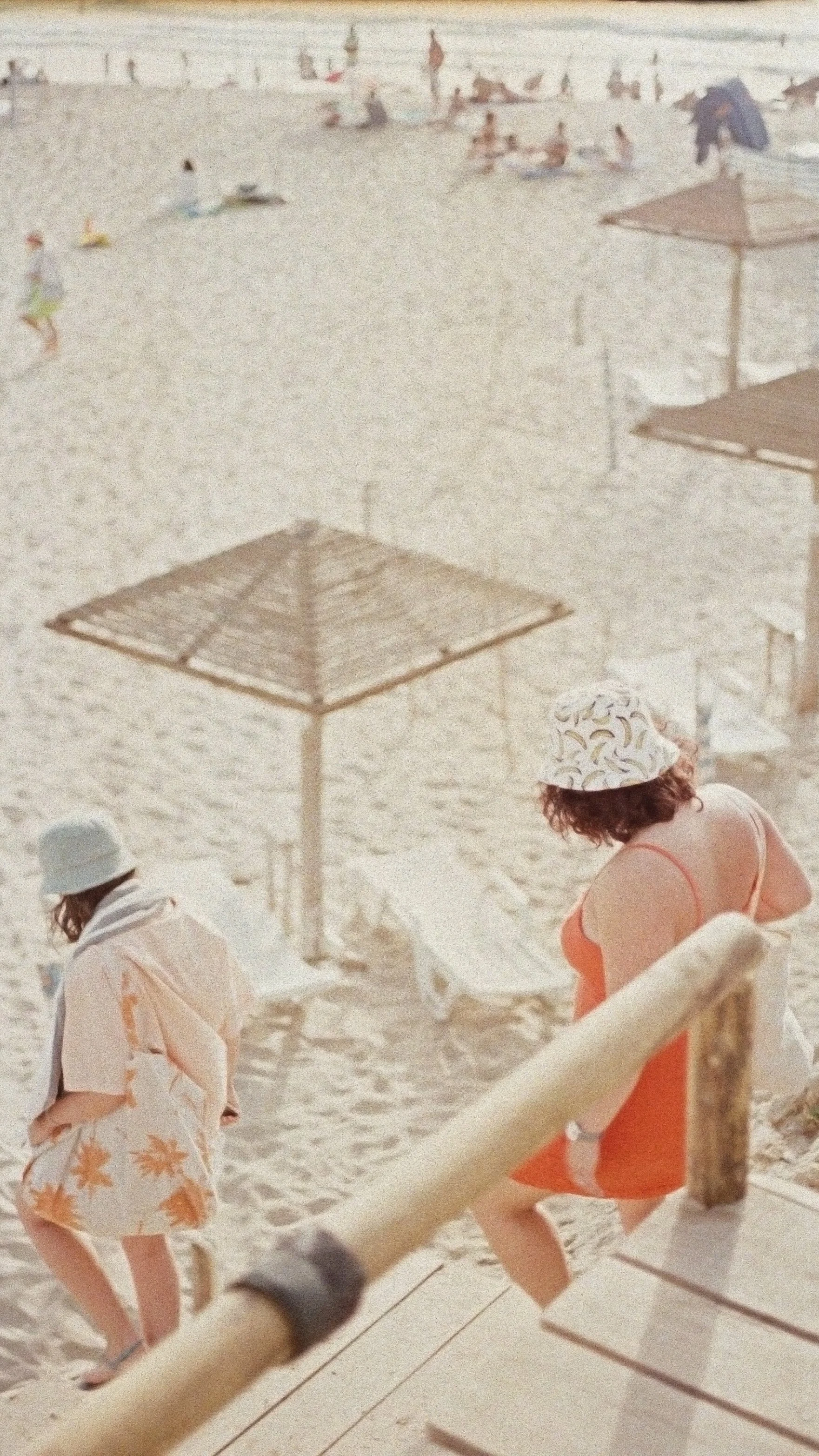 People on a sandy beach under umbrellas, some sitting and some walking, with the ocean in the background.