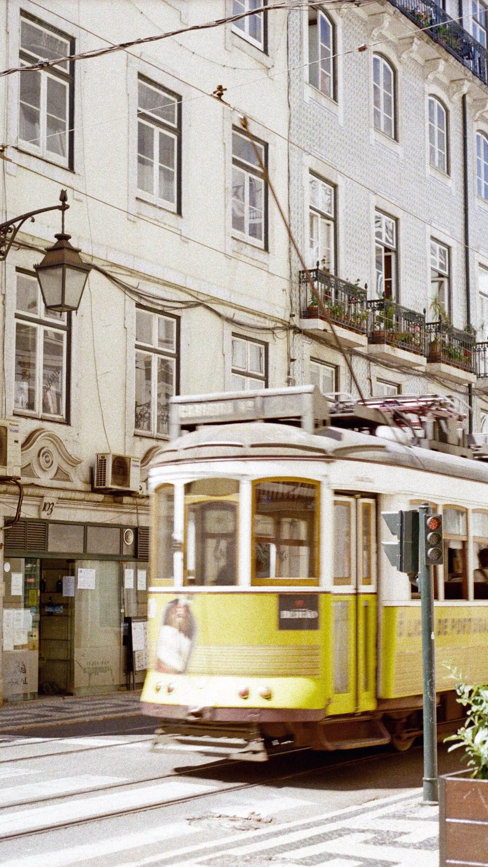 A yellow tram moving through a city street with buildings and balconies in the background.