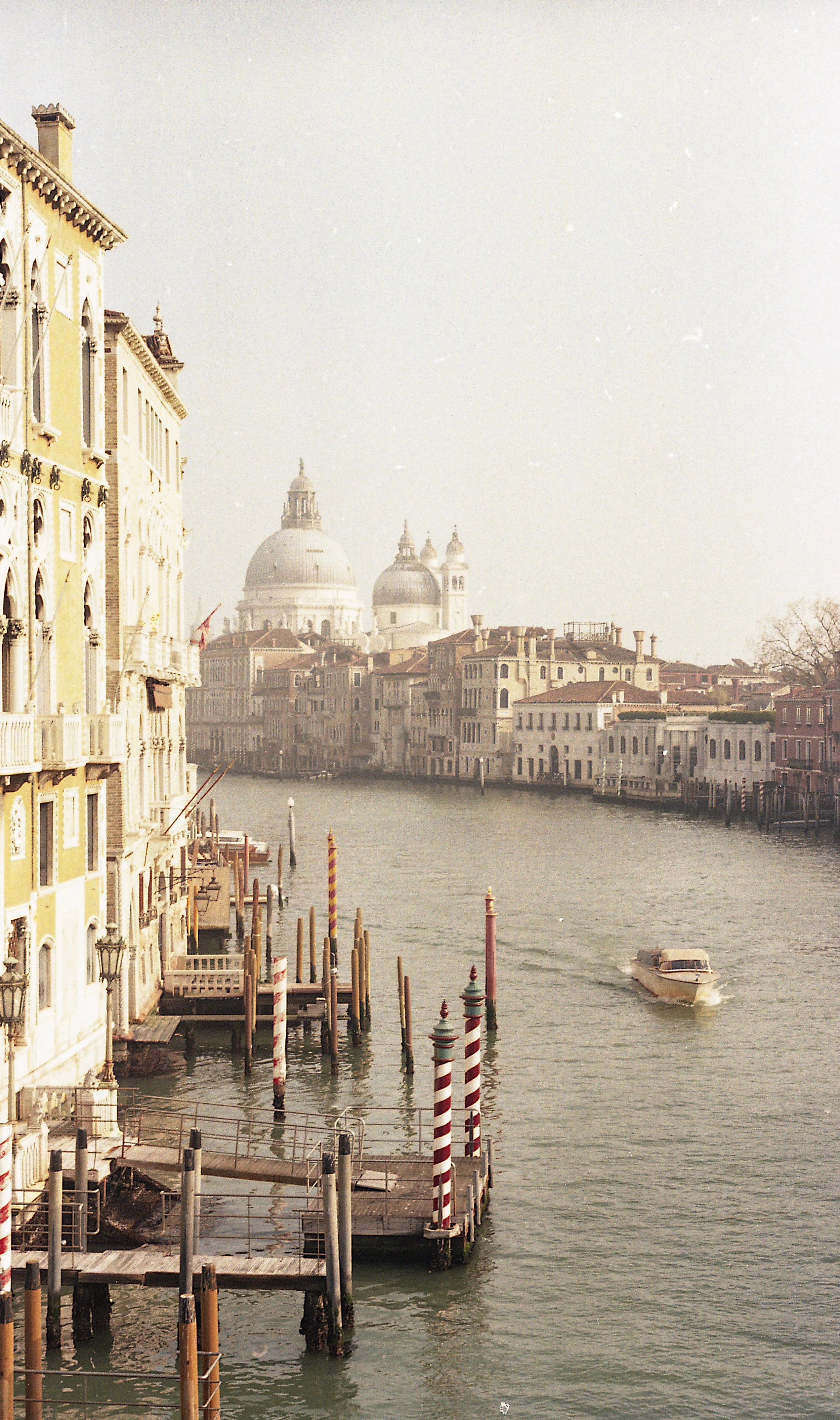 Scenic view of a canal in Venice, Italy, with colorful historic buildings on either side, gondola poles, and a motorboat on the water.