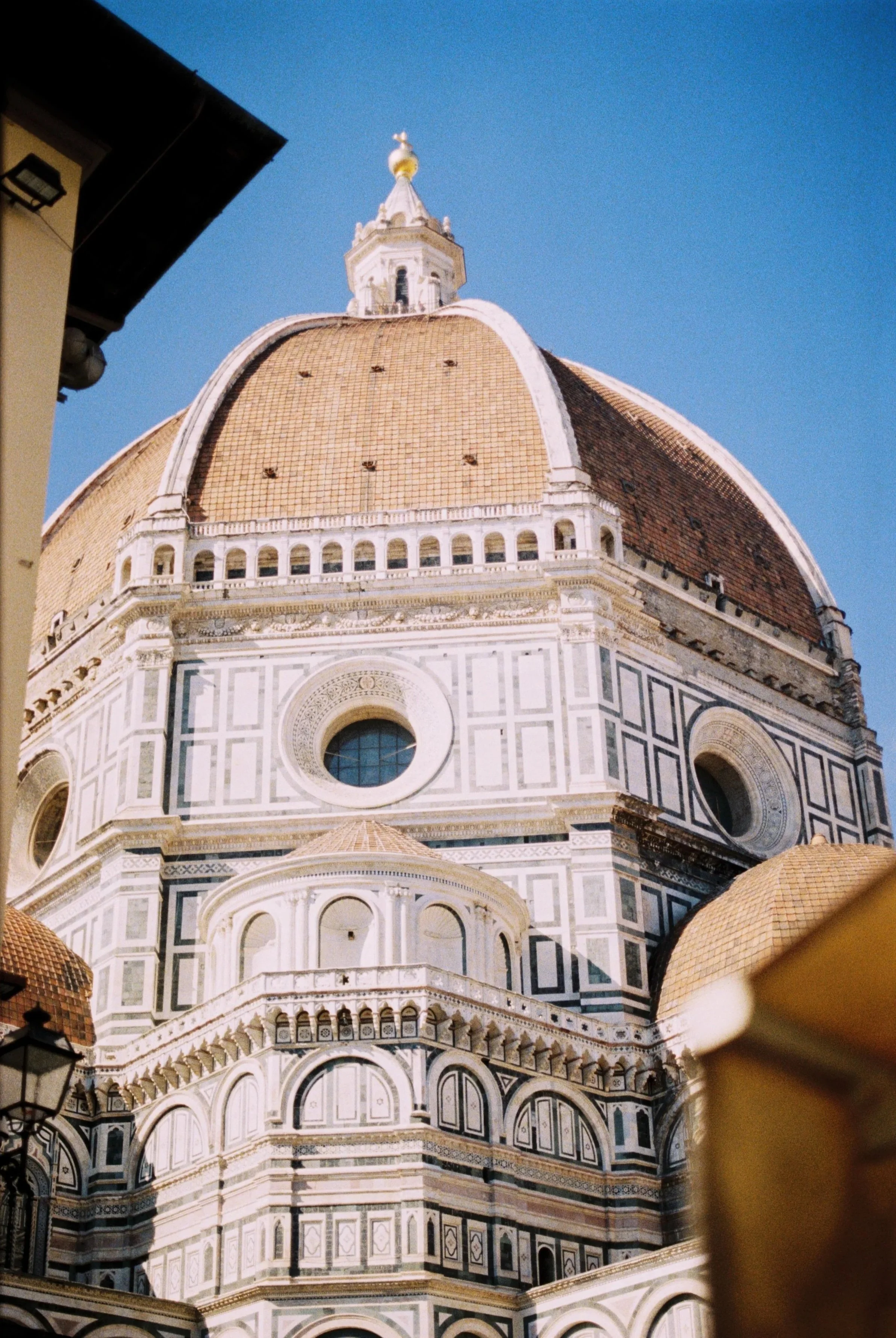 The Florence Cathedral, also known as the Duomo, with its distinctive marble facade and large dome designed by Filippo Brunelleschi, under a clear blue sky.