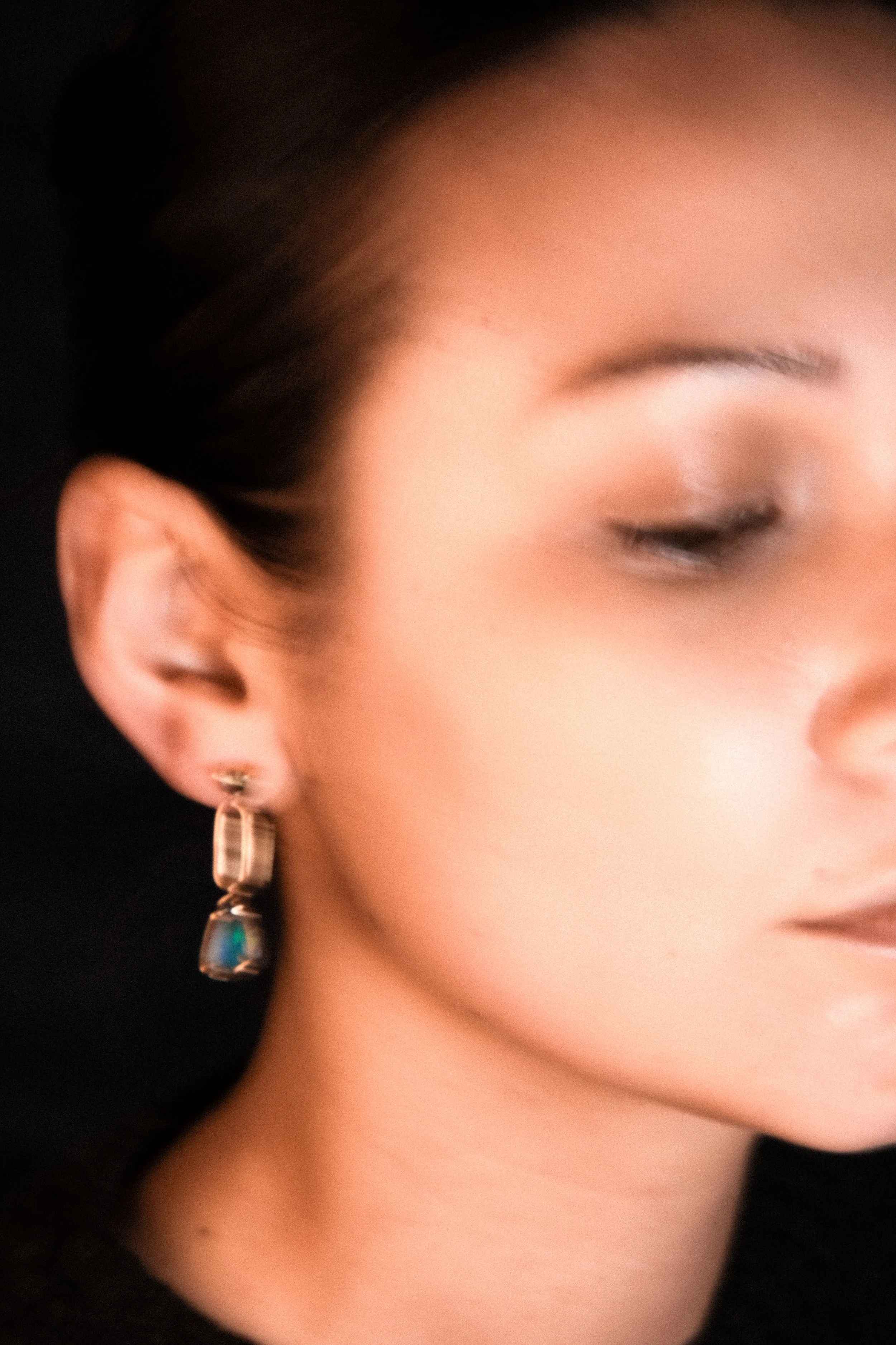 Close-up of a woman with her face turned slightly to the side, showing her ear and earrings, with closed eyes and neutral expression.