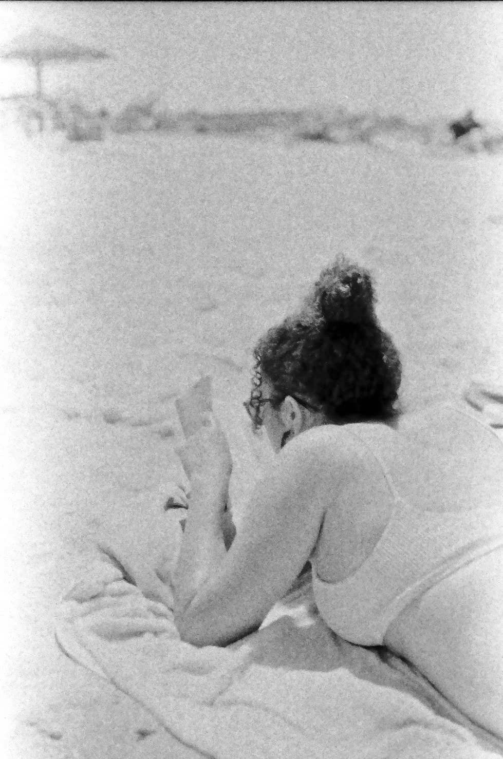A woman with curly hair tied up in a bun, wearing glasses, sitting on the floor and reading a book.