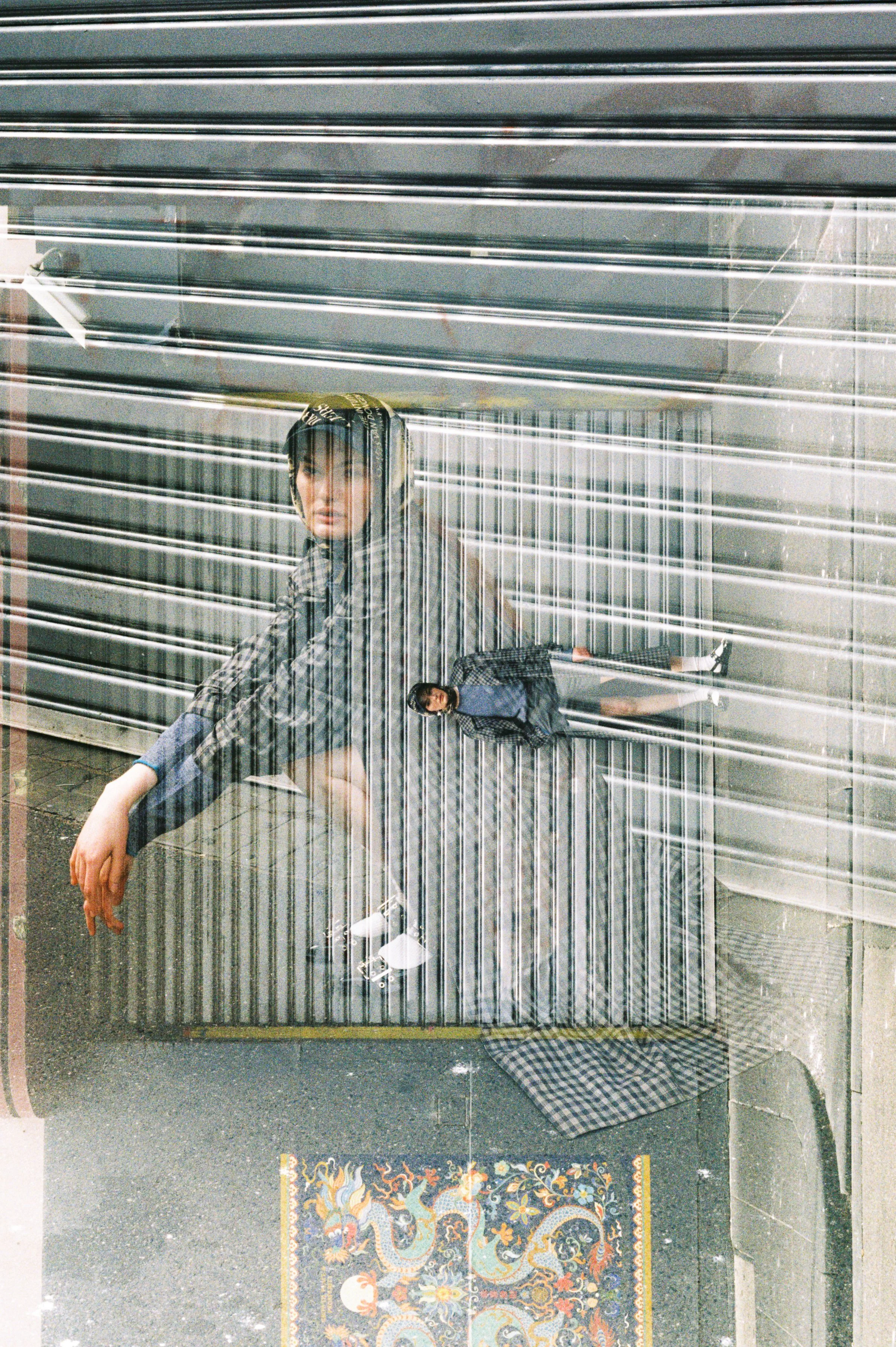 Reflective surface showing a woman leaning on her arm with a man standing nearby, with a multi-colored rug underneath.