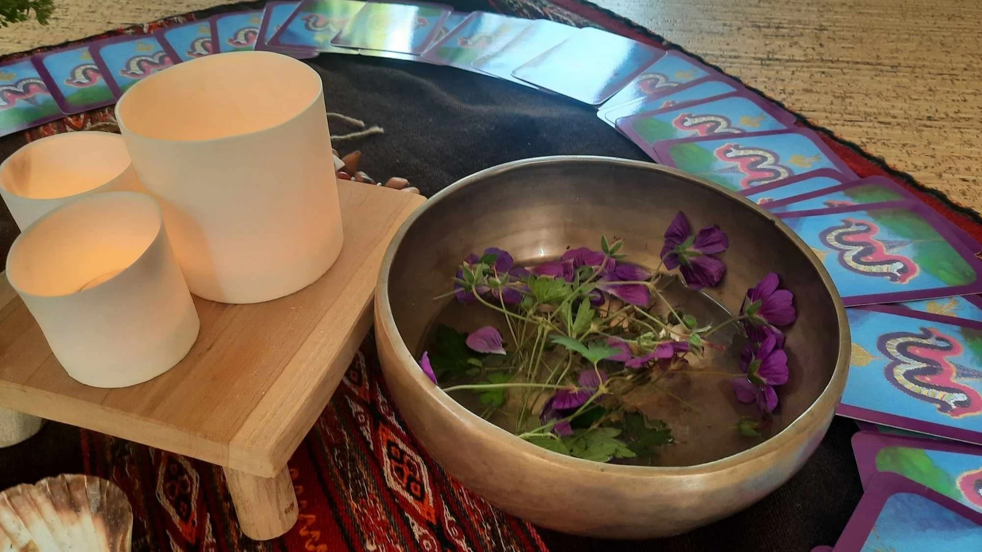 Kalenderkaarten met een slangensymbool, een houten tafel met theelichtjes en een metalen schaal met bloemen en bladeren, op een zwart tafelkleed.