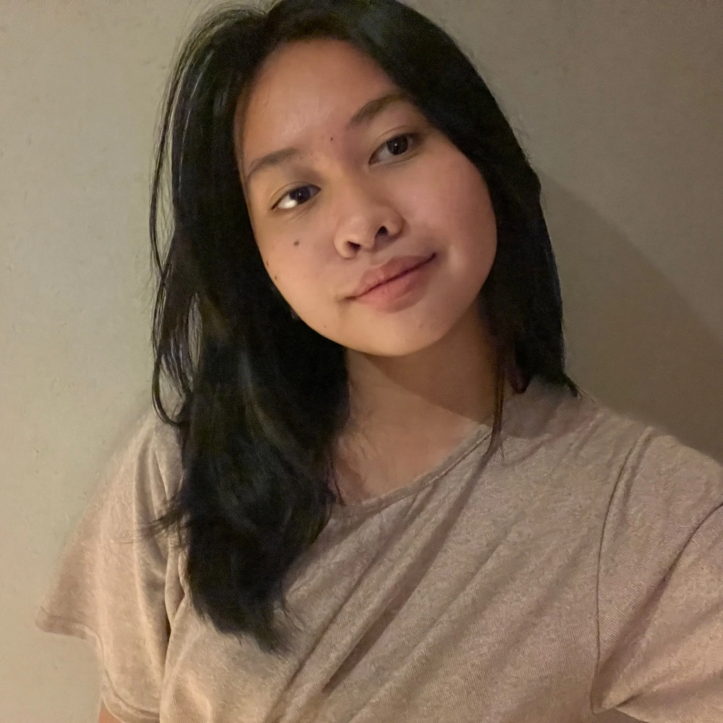 A person with long black hair wearing a light-colored shirt standing against a plain background.