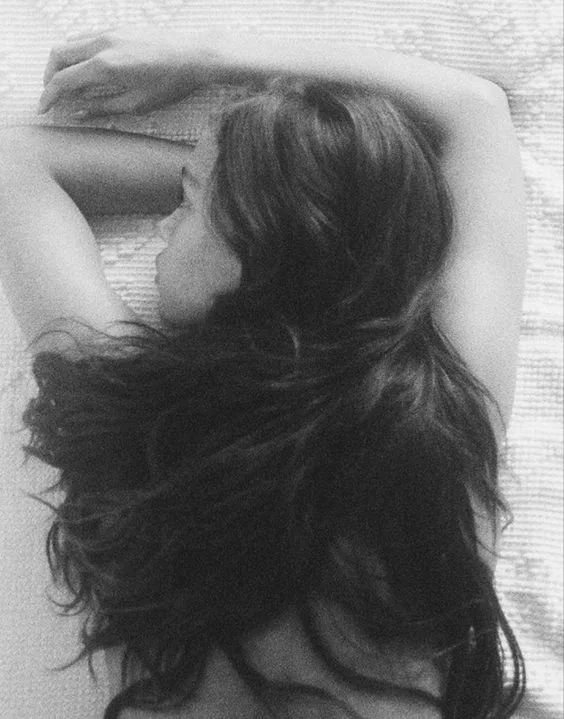 Black and white photo of a person lying face down on a bed, hair spread out on the pillow.