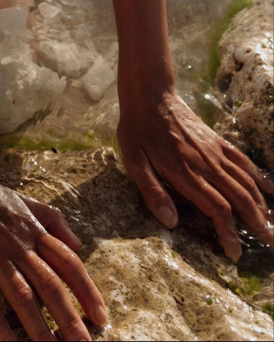 Close-up of two hands touching rocks and water, possibly in a river or stream.