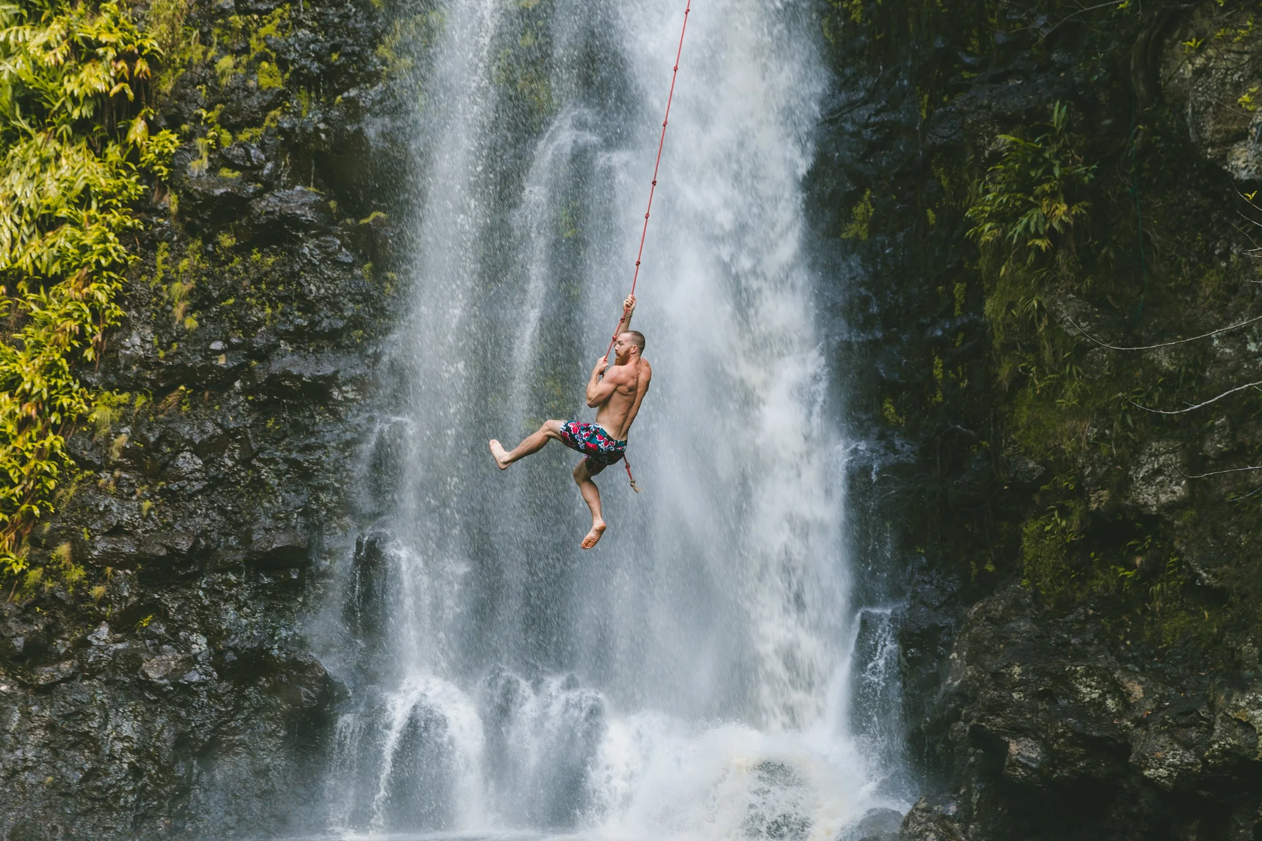 Man die aan een touw hangt voor een waterval in Paraguay met groene vegetatie op de achtergrond.