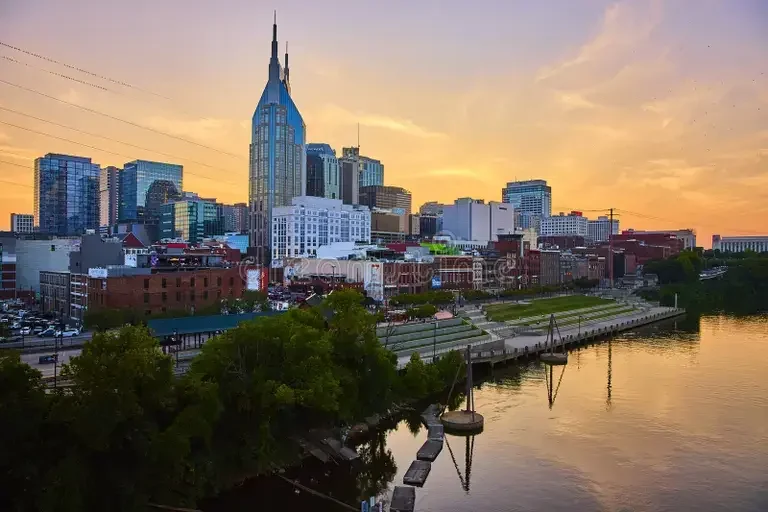 nashville-skyline-sunset-riverfront-reflections-elevated-view-golden-hour-bathes-iconic-warm-glow-batman-building-336403760.webp