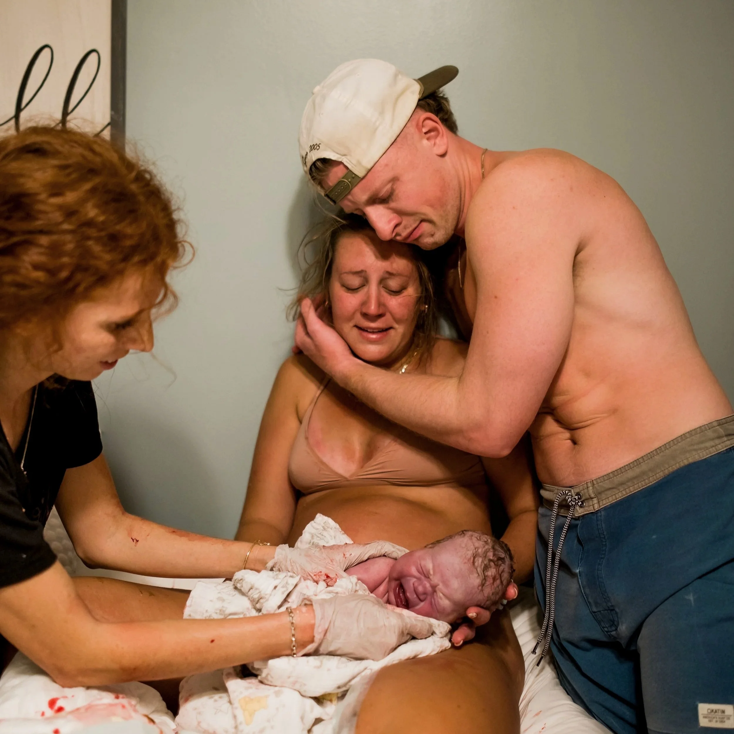 A woman delivering a baby in a bedroom with assistance the midwife and her husband holder her.