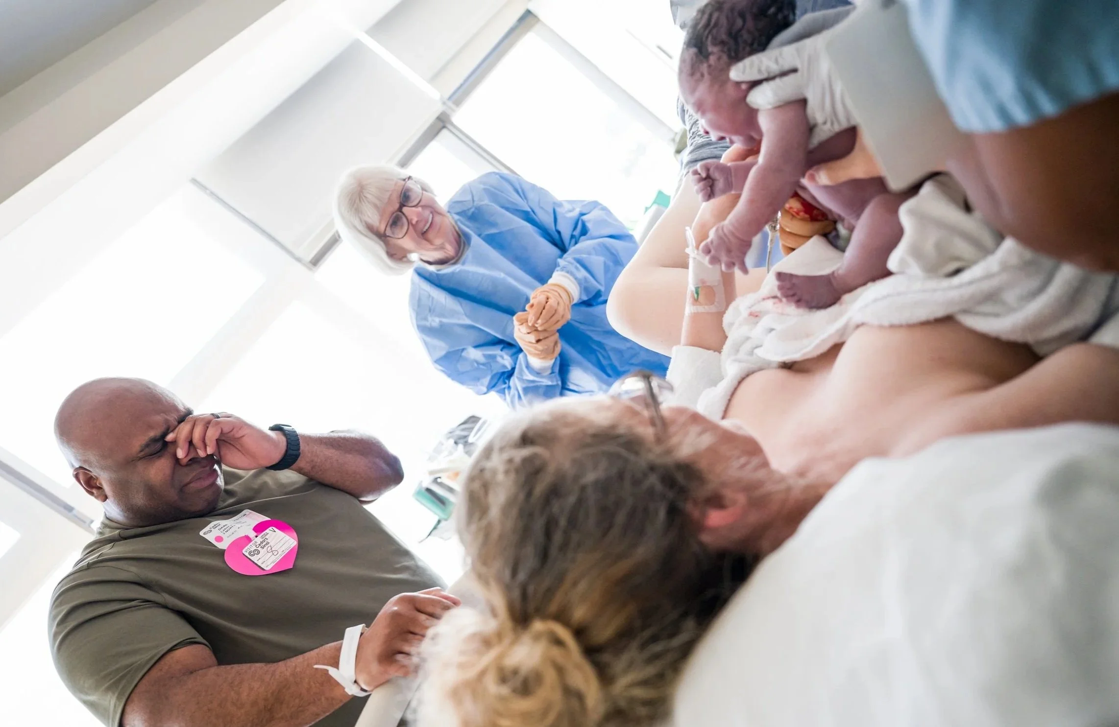 dad getting emotional after his wife had his baby and he meets her face to face. Grandma in the background smiling and looking at her newest grand baby.