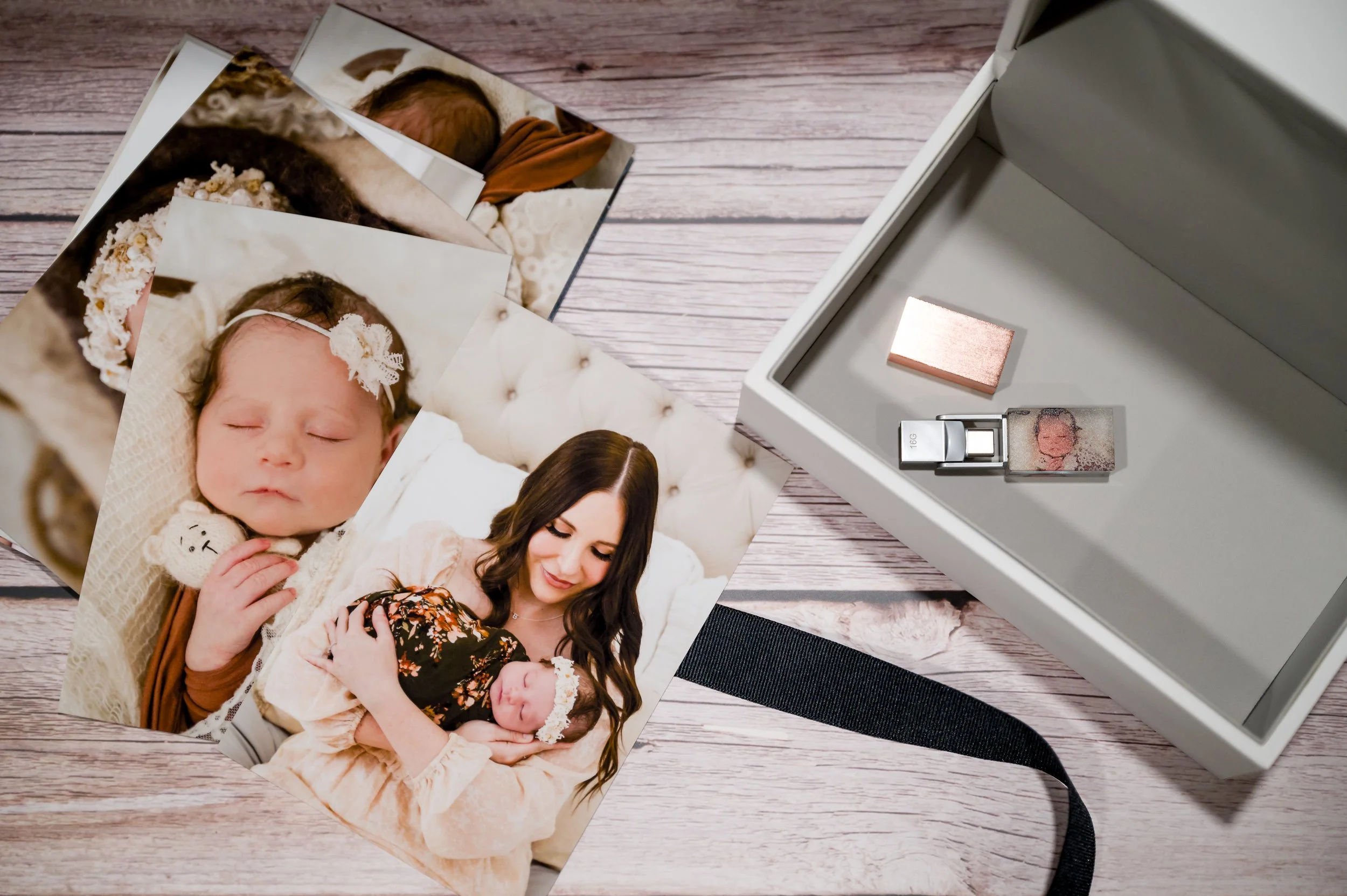 Prints of photos of a woman and two babies on a wooden surface next to an open photo box with a custom usb.