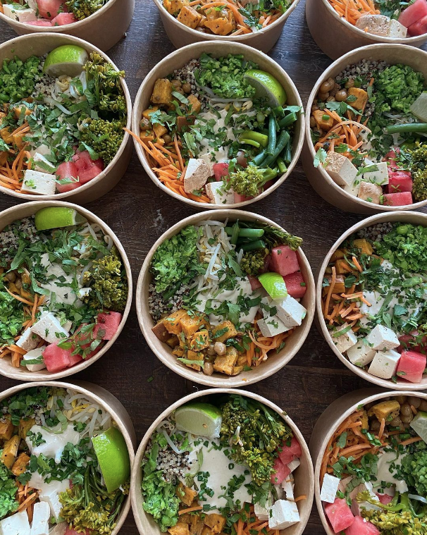 Multiple bowls filled with colorful vegan salads including vegetables, tofu, lime wedges, and grains, arranged on a wooden surface.