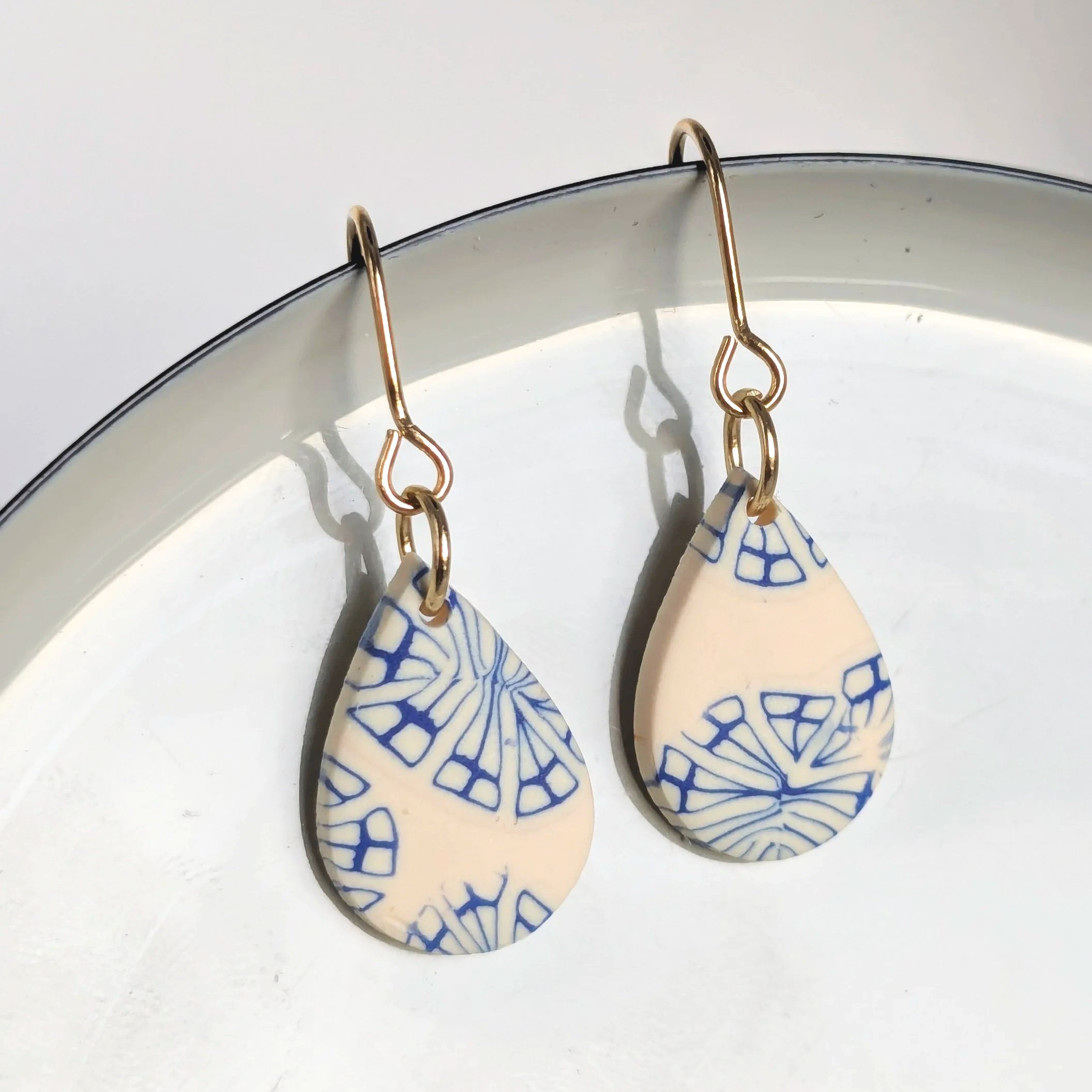 Pair of teardrop-shaped earrings with blue geometric patterns on a white background, hanging from gold hooks.