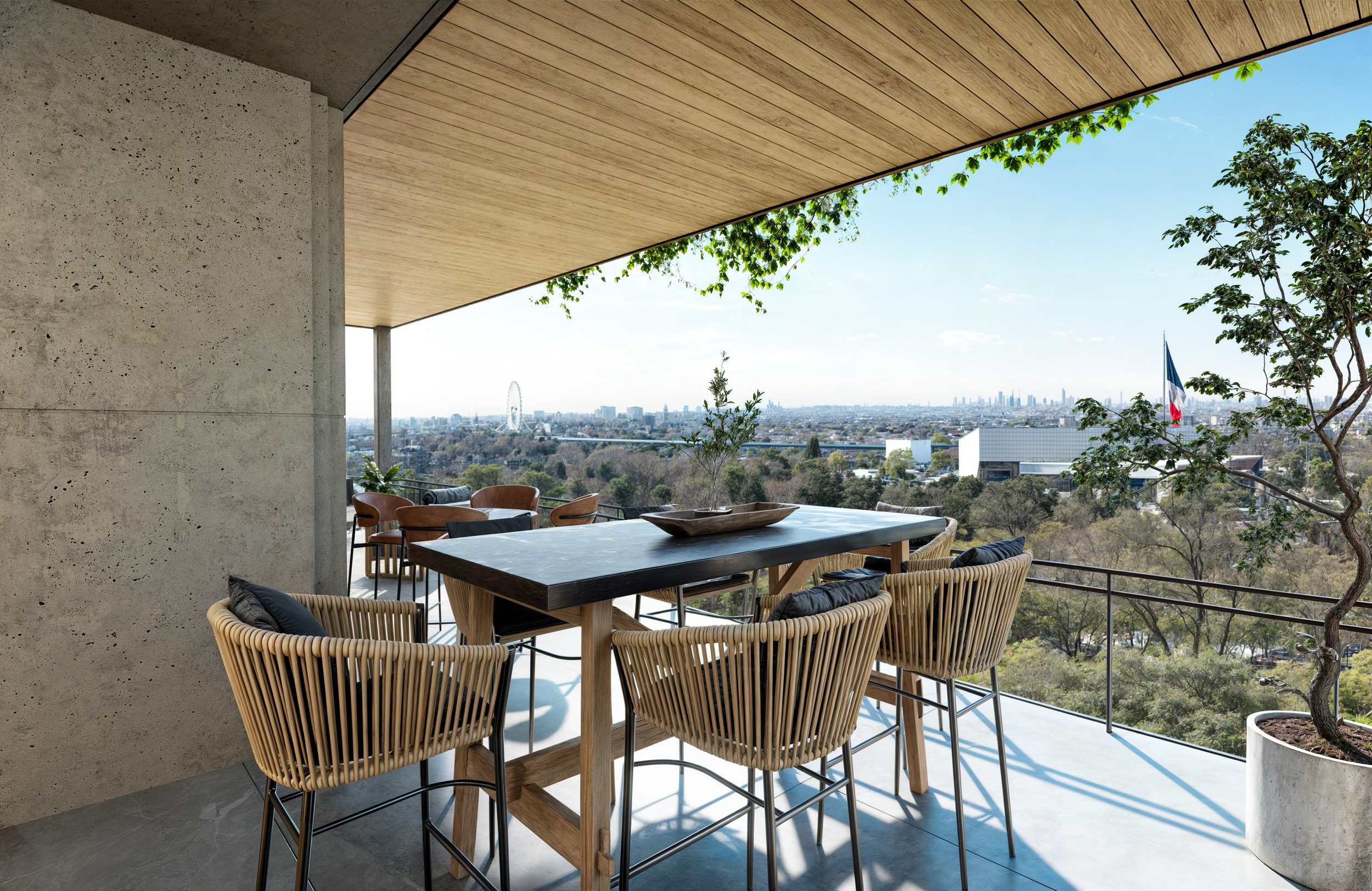 Terraza moderna con mesa de madera y sillas de mimbre, vista panorámica de la ciudad, árboles y bandera francesa.