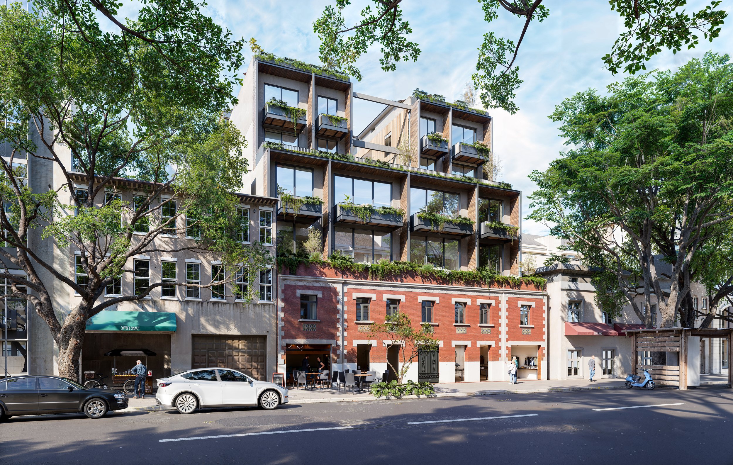 Edificio moderno de departamentos con balcones con plantas, fachada de ladrillo y estructura de concreto, rodeado de árboles en una calle urbana con autos y personas caminando