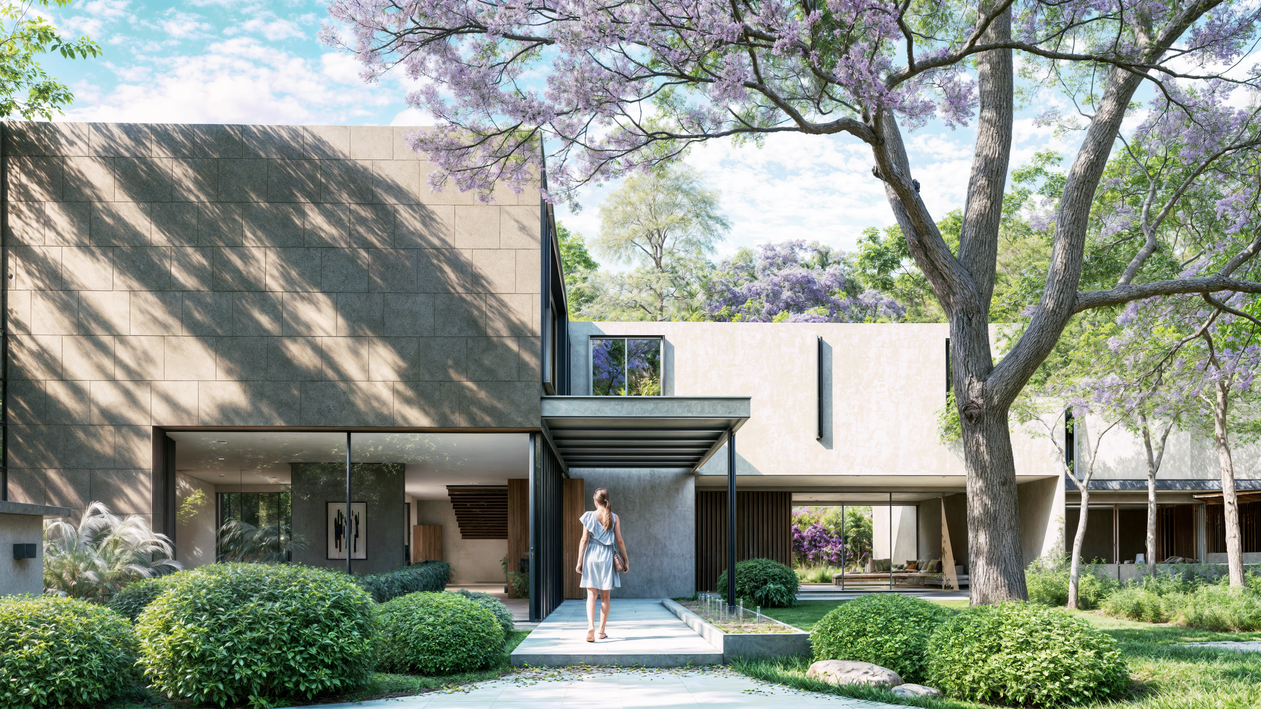 Vista exterior de una casa moderna rodeada de un jardín verde con árboles y arbustos, con una mujer caminando hacia la entrada en un día soleado.