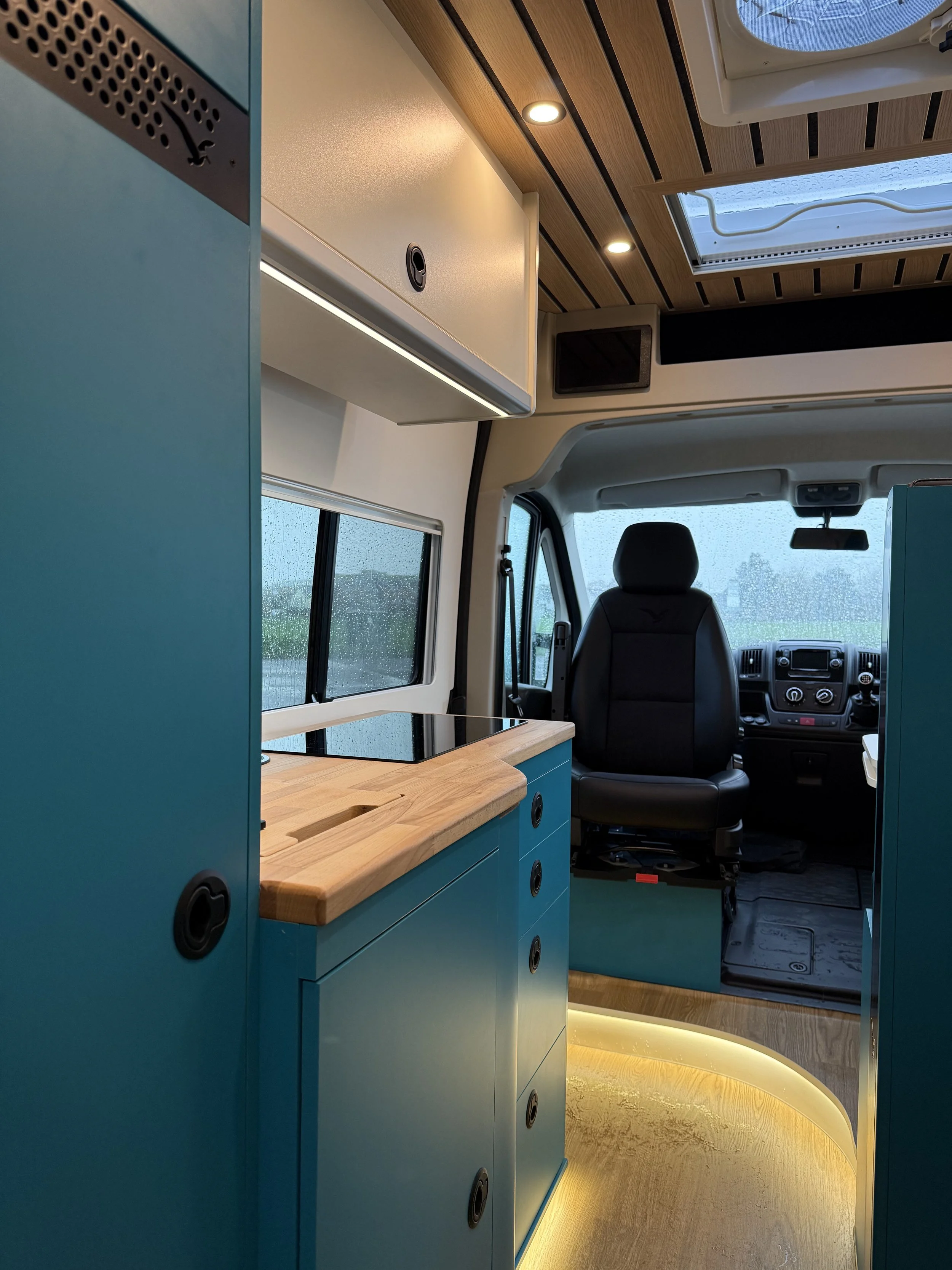 Interior of the Albatross Conversions Roam Edition campervan featuring a modern custom kitchen with curved wood countertop and a sleek black induction stovetop.