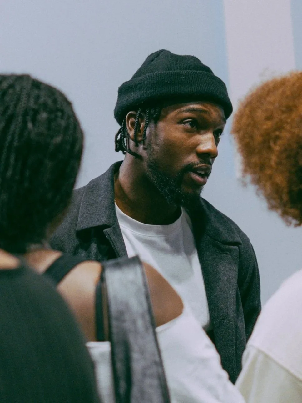 Supacell actor Tosin Cole wearing a black beanie, and a beard, engaged in conversation with two women, one with curly red hair and the other with braids, at a private masterclass.
