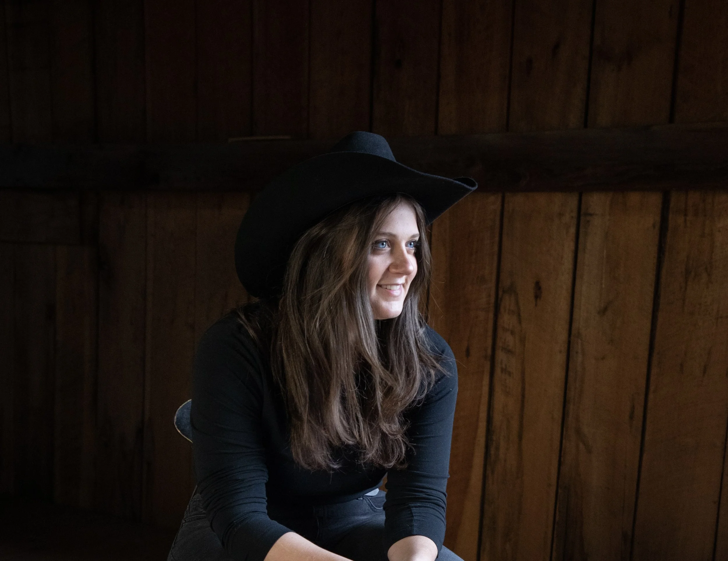 Woman in a cowboy hat smiling inside a wooden cabin.