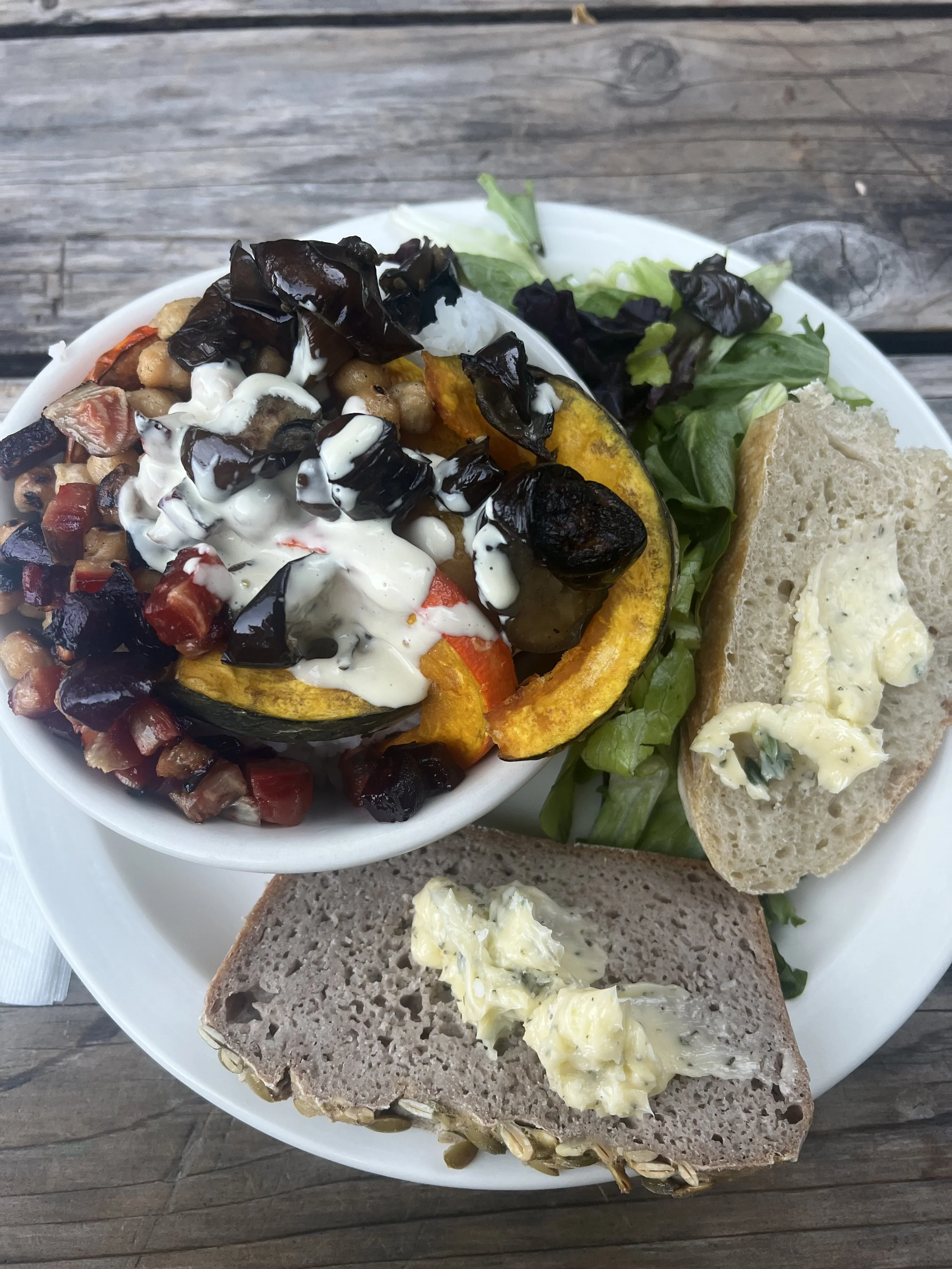 Plate of food with roasted vegetables, salad, bread with butter, and a side dish with a grain and cheese.