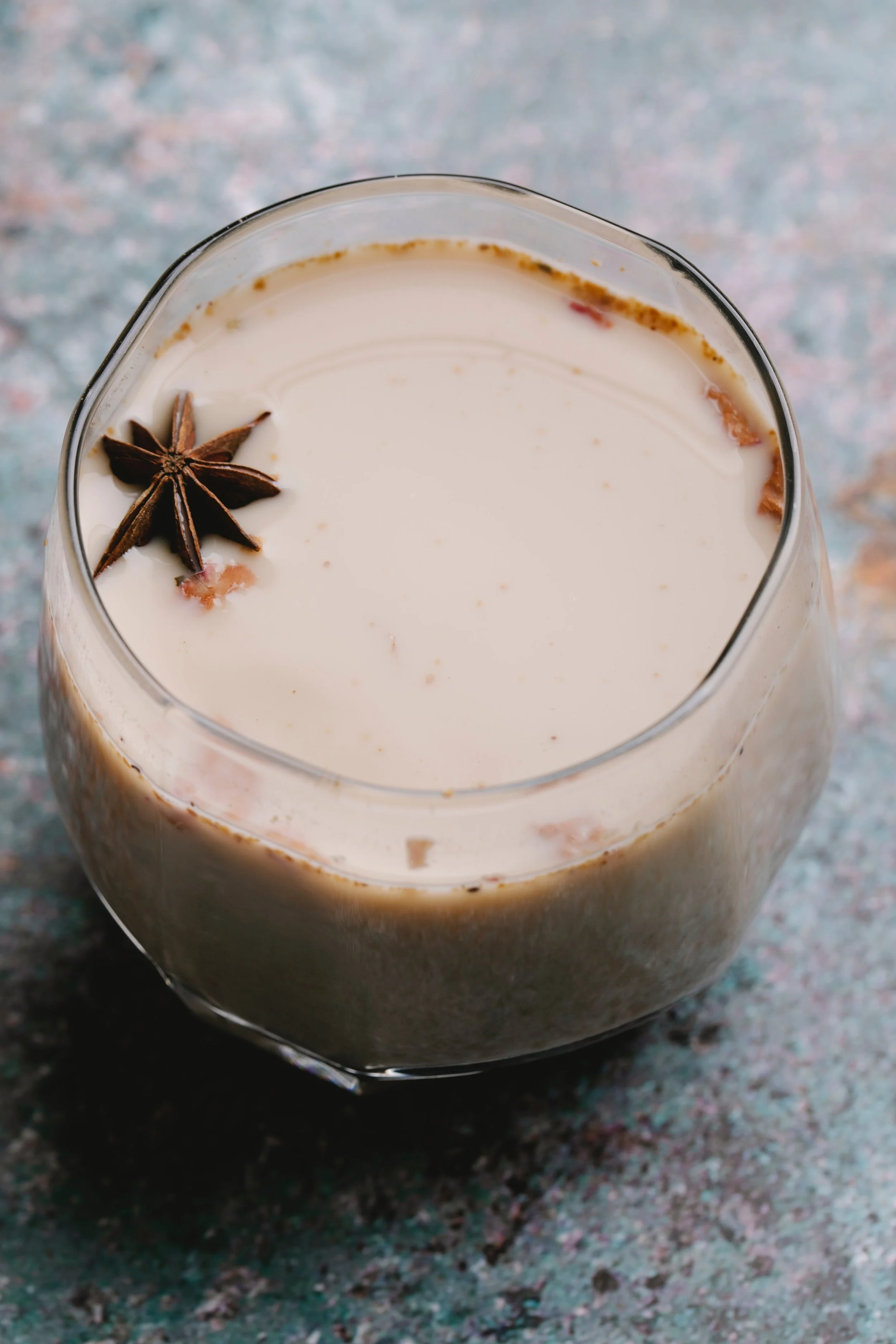 A glass of eggnog garnished with star anise on top, on a textured surface.