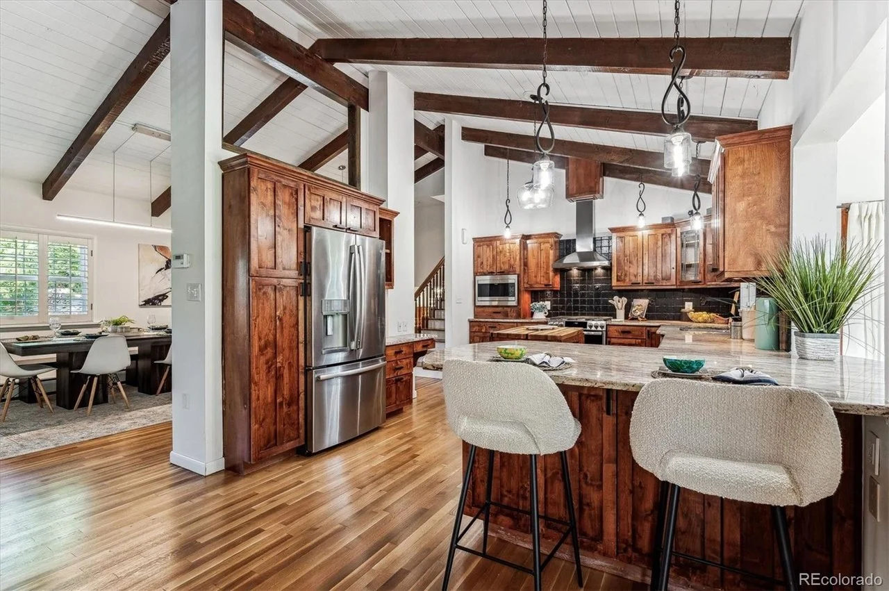 Rustic kitchen interior with wooden cabinets, stainless steel appliances, island with barstools, and exposed wooden beams.