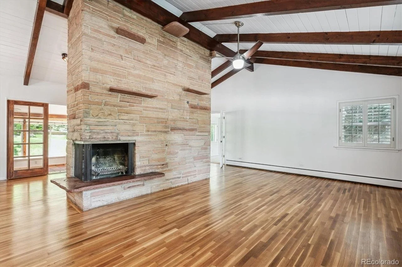 Spacious living room with wood floors, stone fireplace, vaulted ceiling, exposed wooden beams, and ceiling fan.