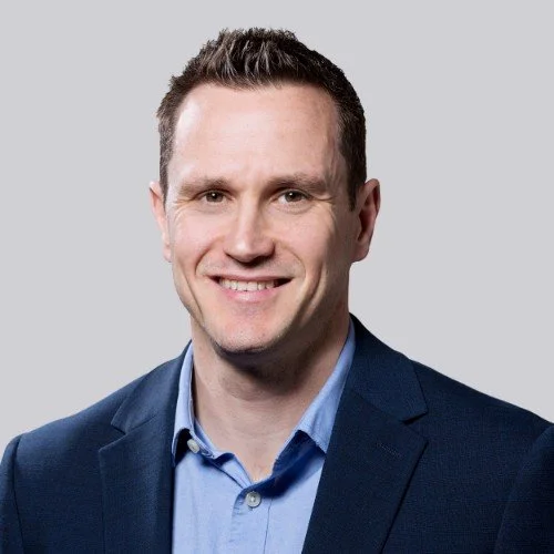 Colour portrait style photo of a smiling man in a dark blue suit.