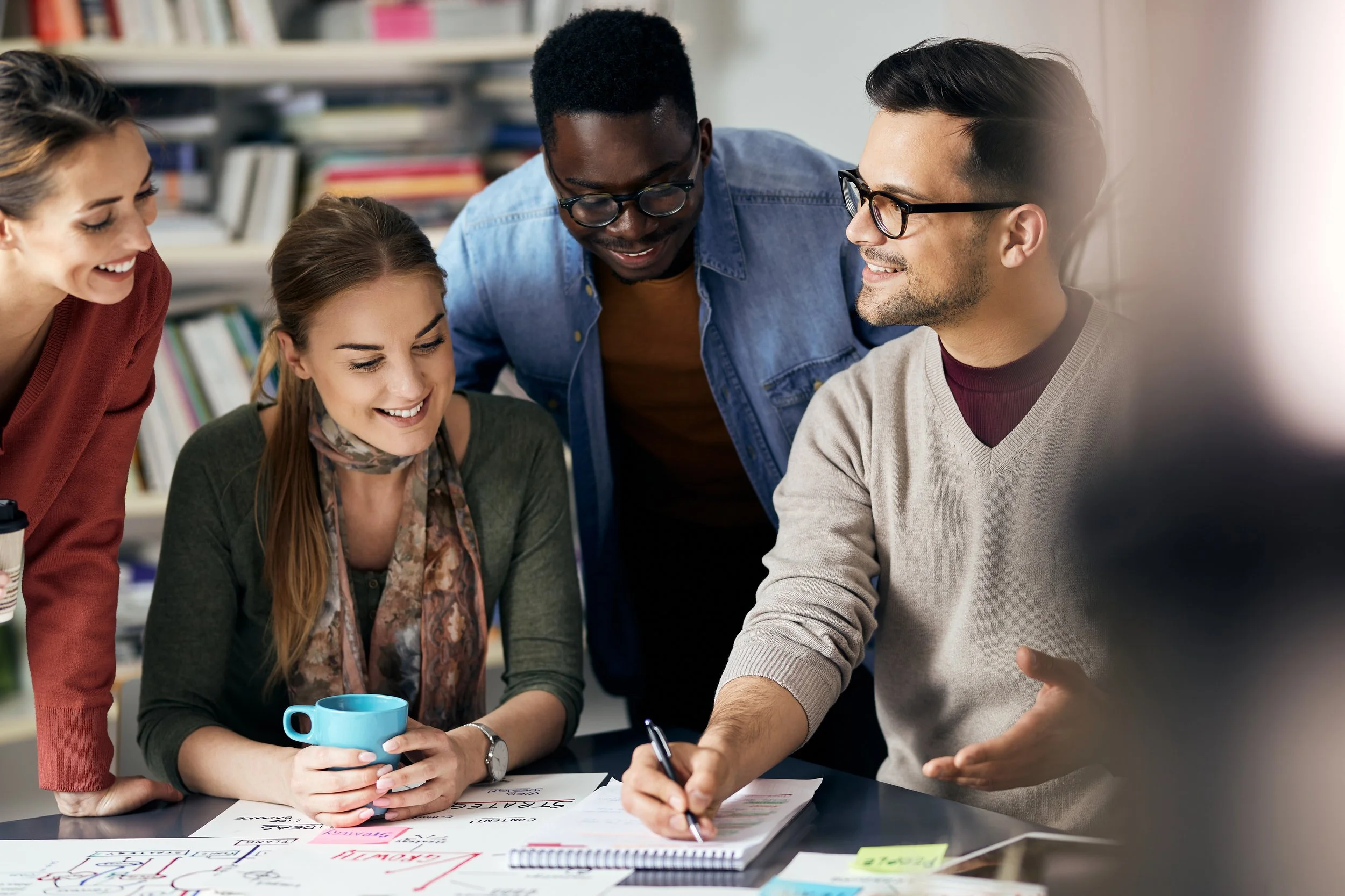 Colour photo of three people talking while writing on a small white paper notepad.