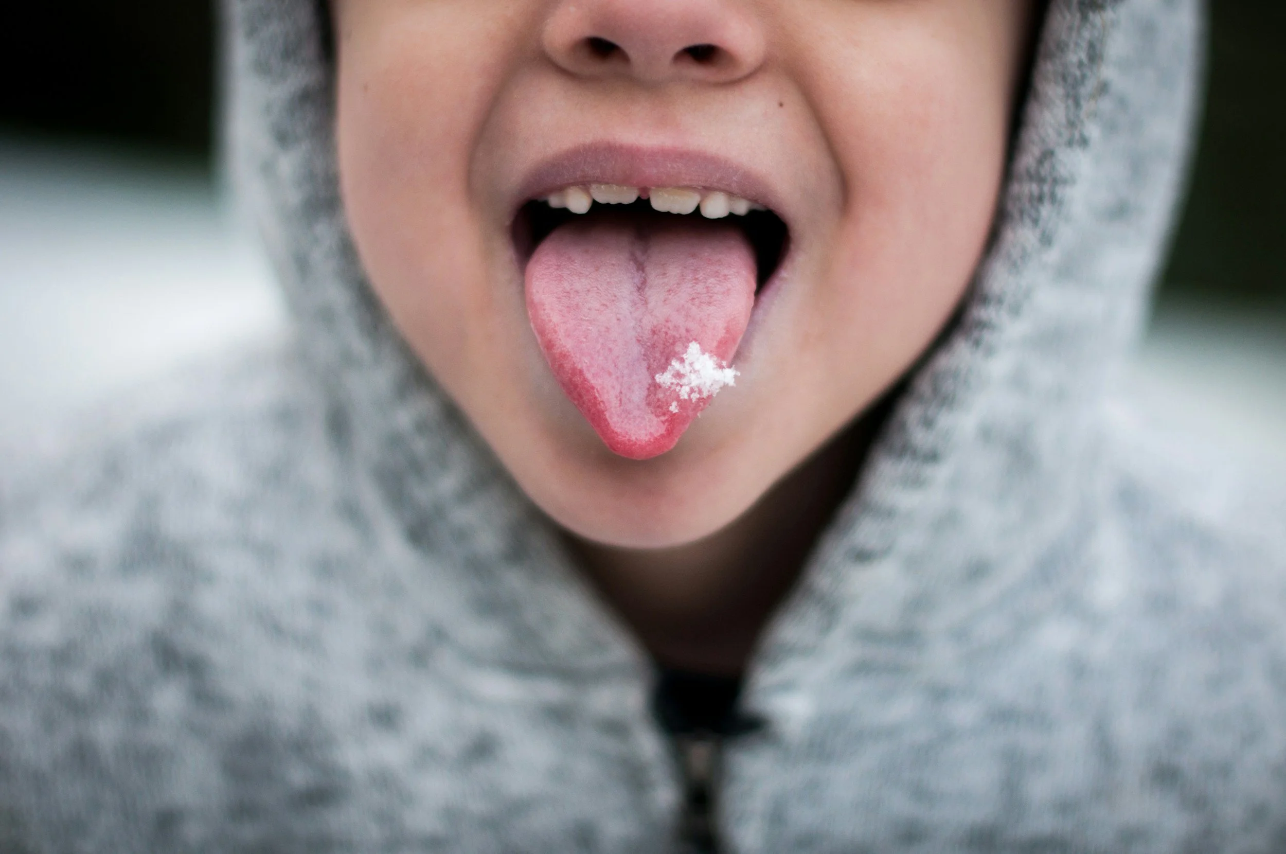 A person sticking out their tongue with some white powder on it, wearing a gray hoodie.