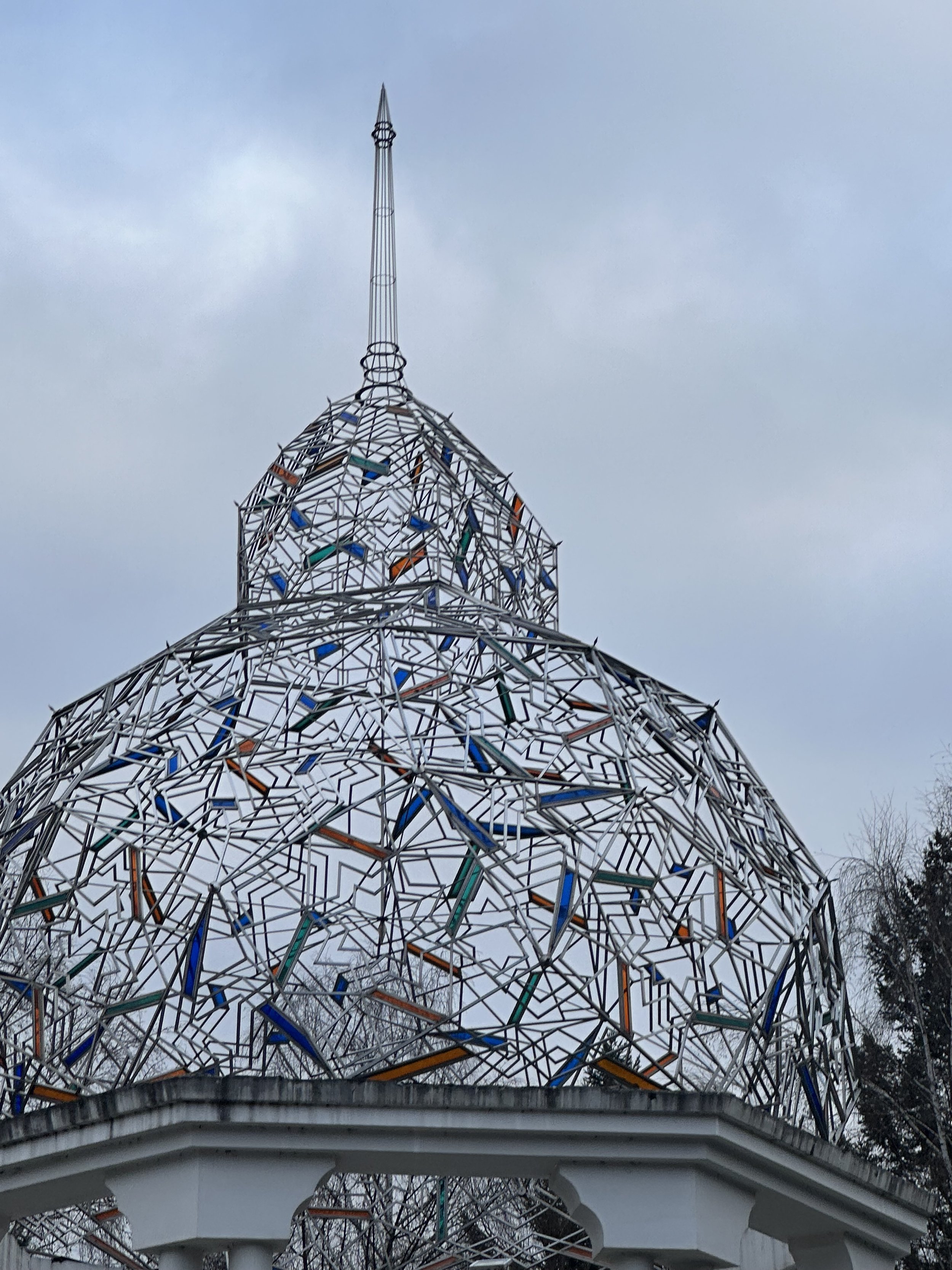 Dome-shaped metal structure with colorful geometric patterns on a cloudy day.