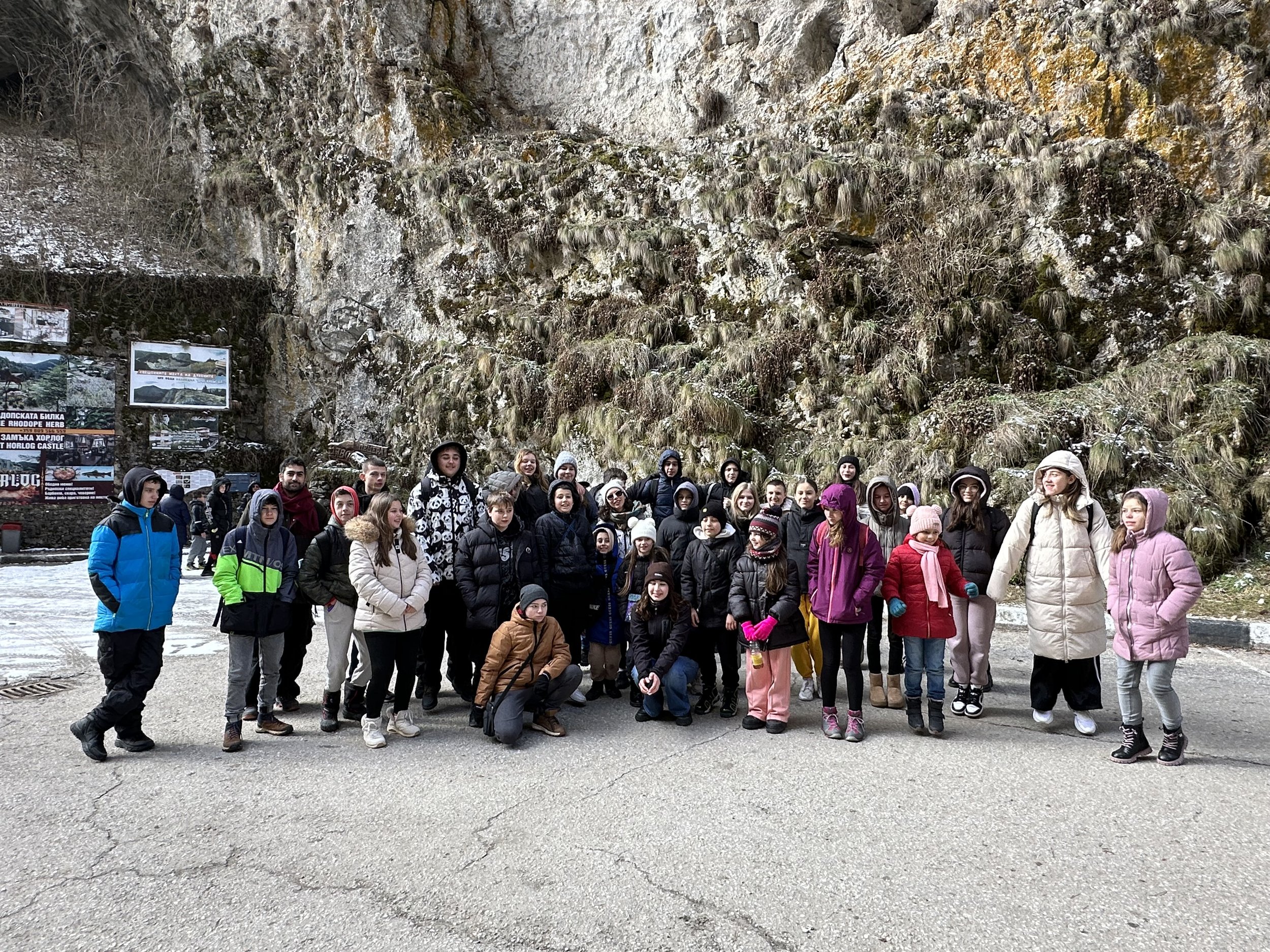 Group of people in winter clothing standing outdoors near a rocky, moss-covered cliff.