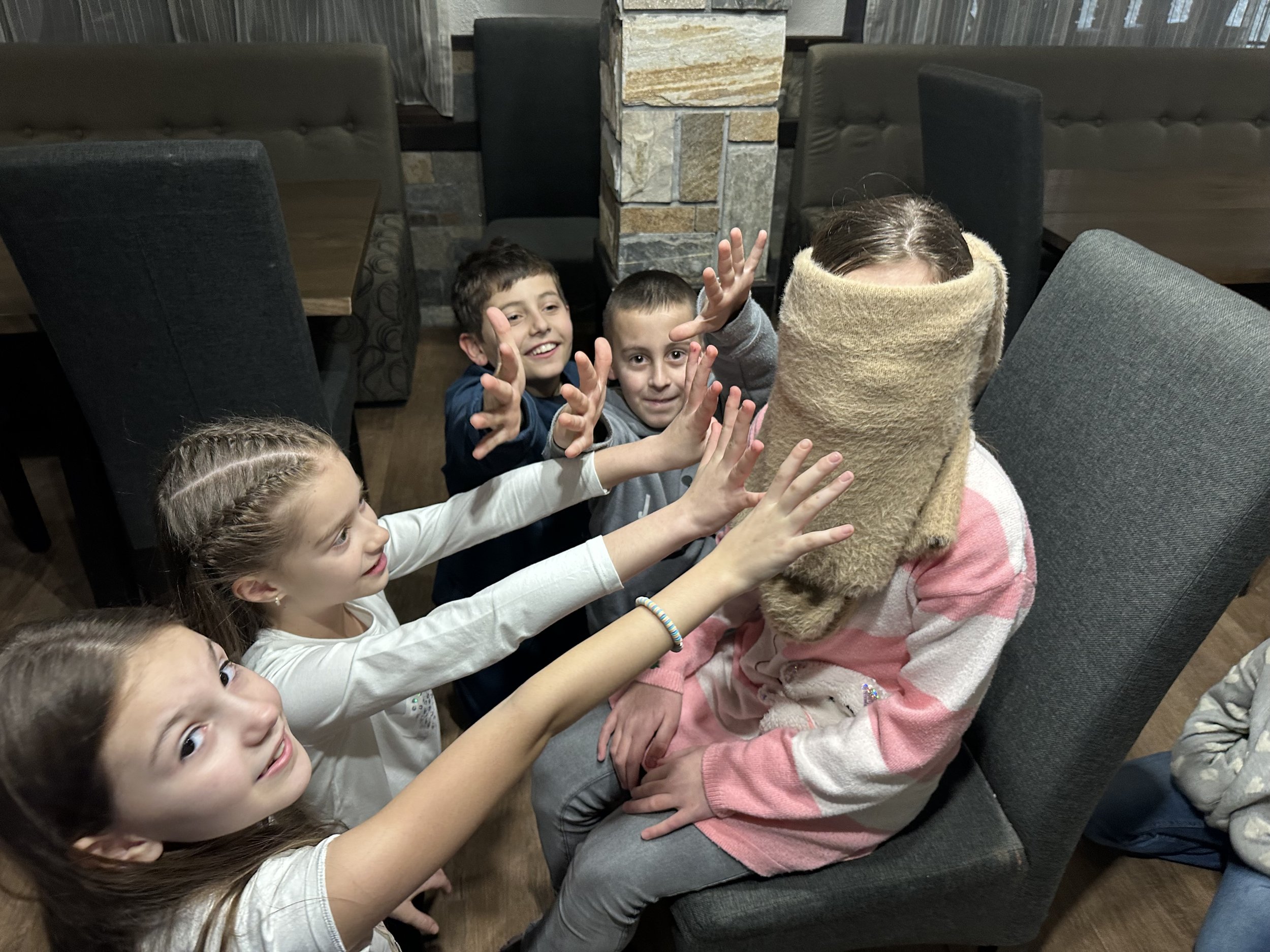 Group of children playing a game indoors with one child blindfolded.