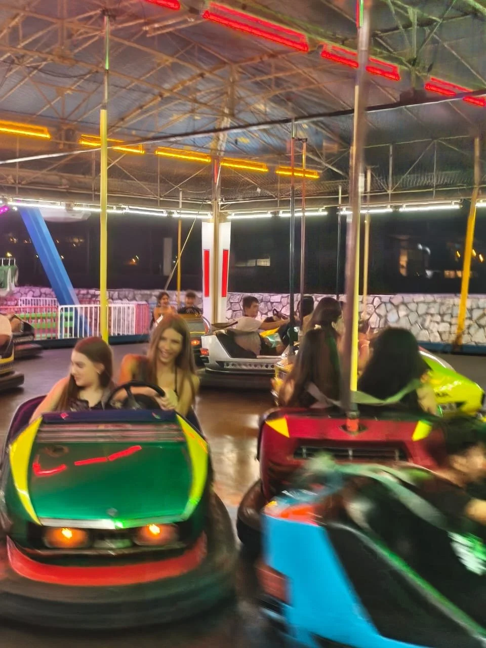 Children at Camp Evolve International enjoying bumper cars during an evening visit to the lunar park in Kavala, Greece, surrounded by colourful lights and a lively amusement park atmosphere at night
