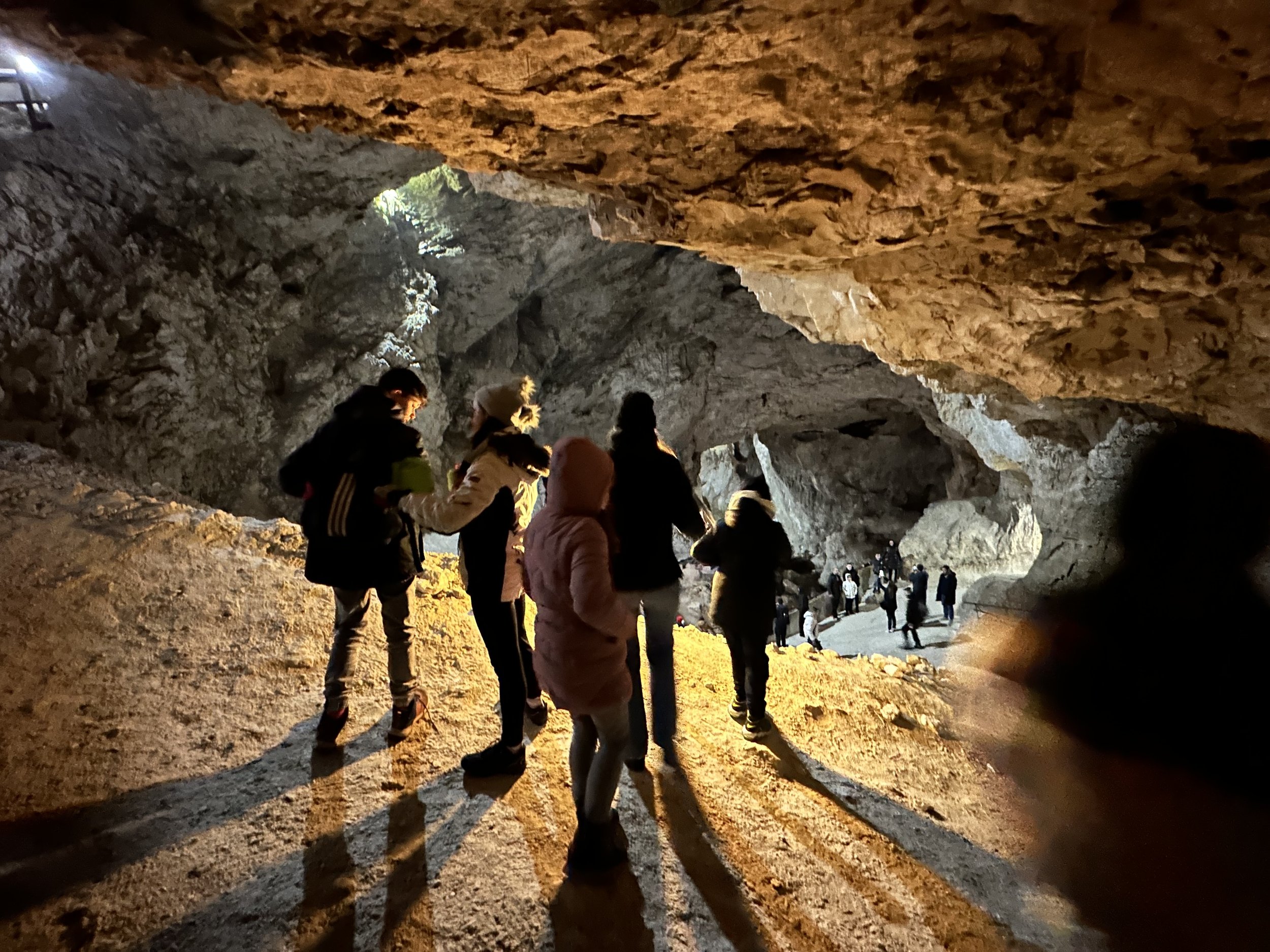 People exploring inside a large, rocky cave with dim lighting.