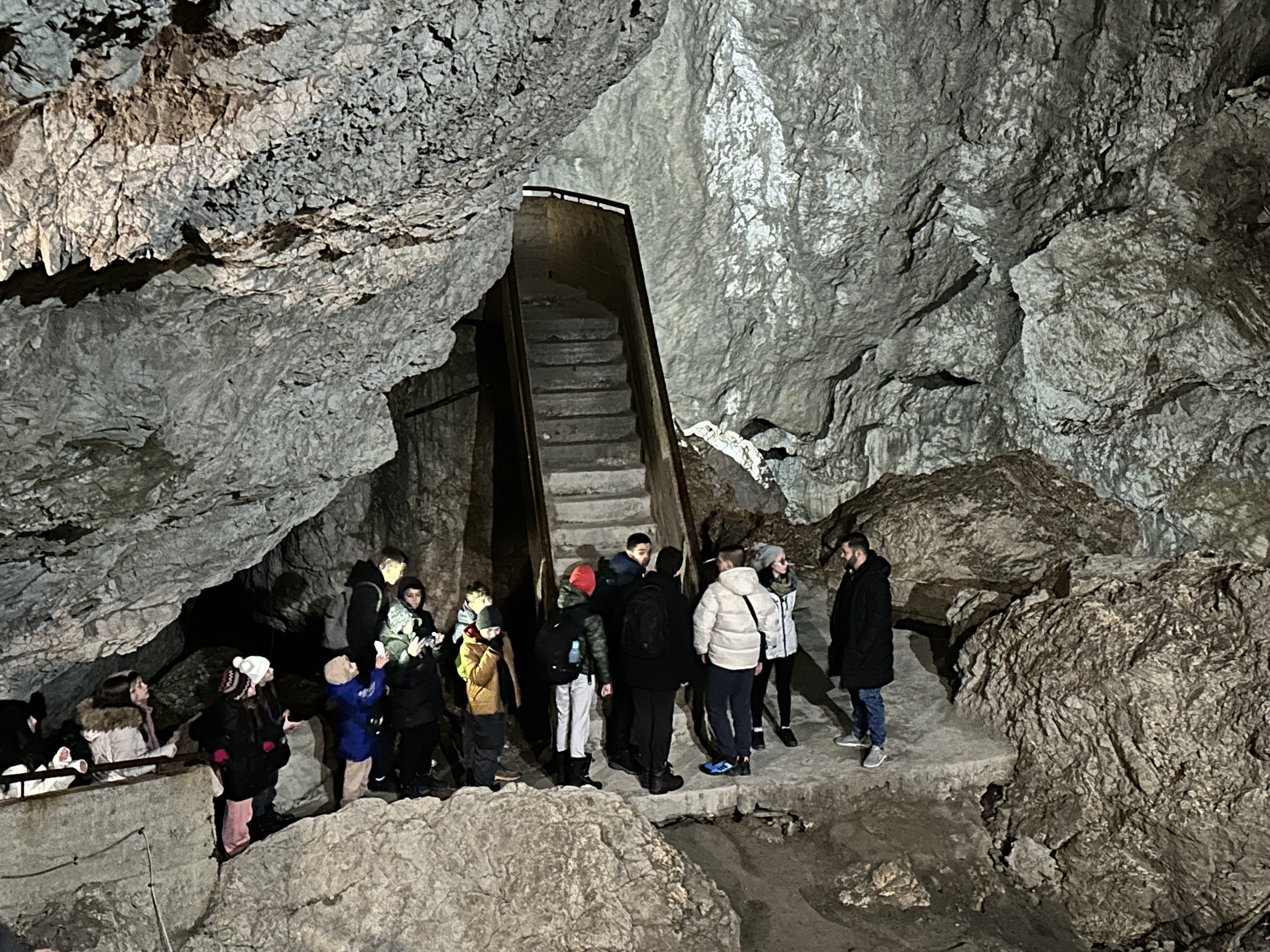 A group of people exploring a large cave interior with a rock staircase.